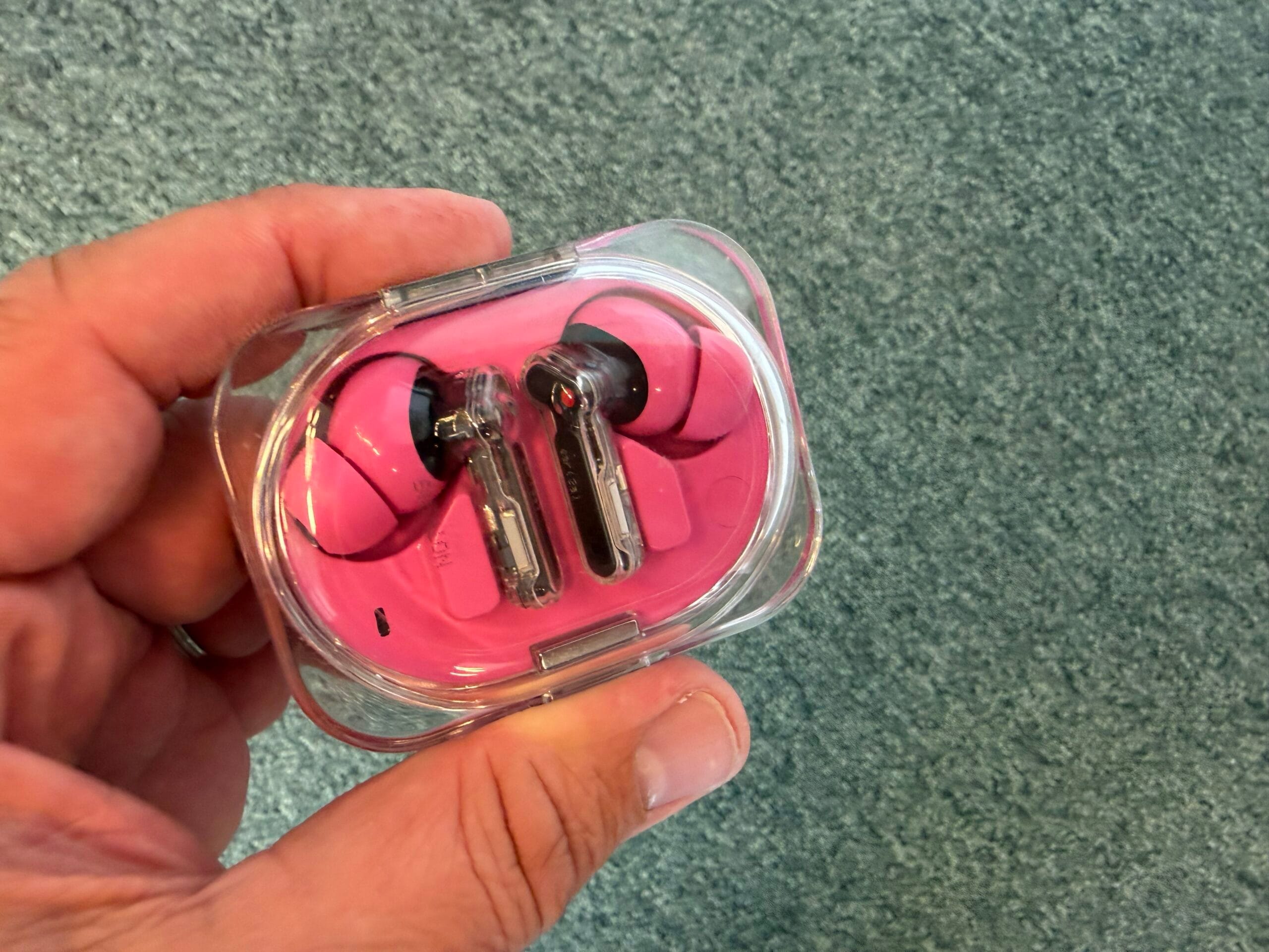 Roze Nothing Ear (3a) oordopjes in een compacte, transparante oplaadcase vastgehouden in een hand