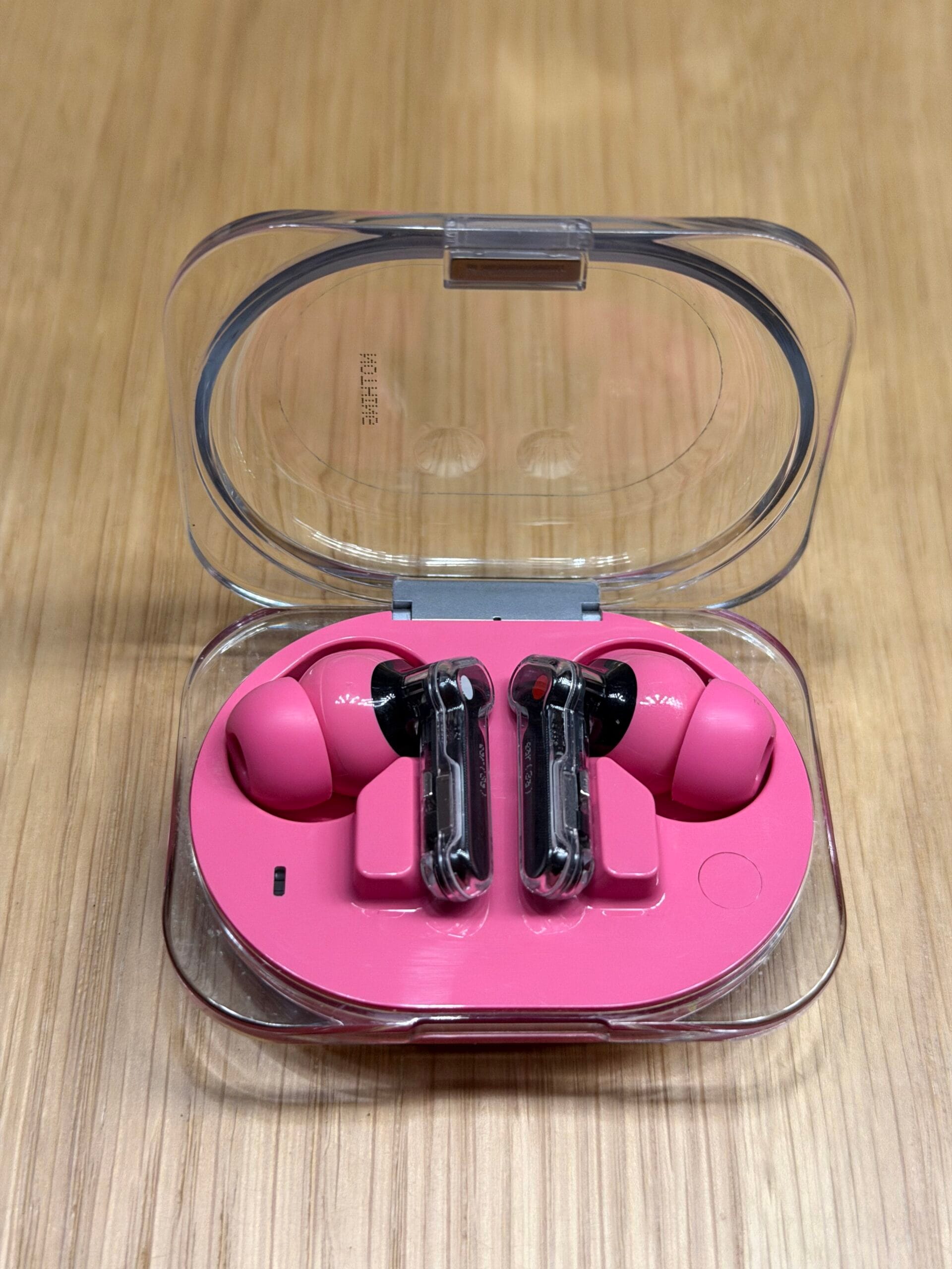 Roze Nothing Ear (3a) oordopjes in een compacte, transparante oplaadcase op een houten ondergrond
