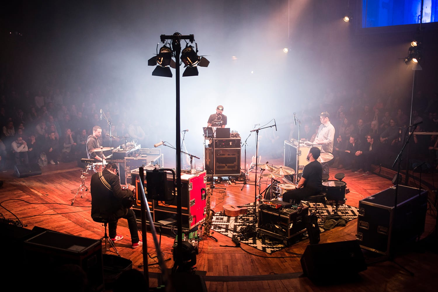 Muzikanten treden op in een cirkel op een houten podium omringd door publiek tijdens het PEOPLE Festival