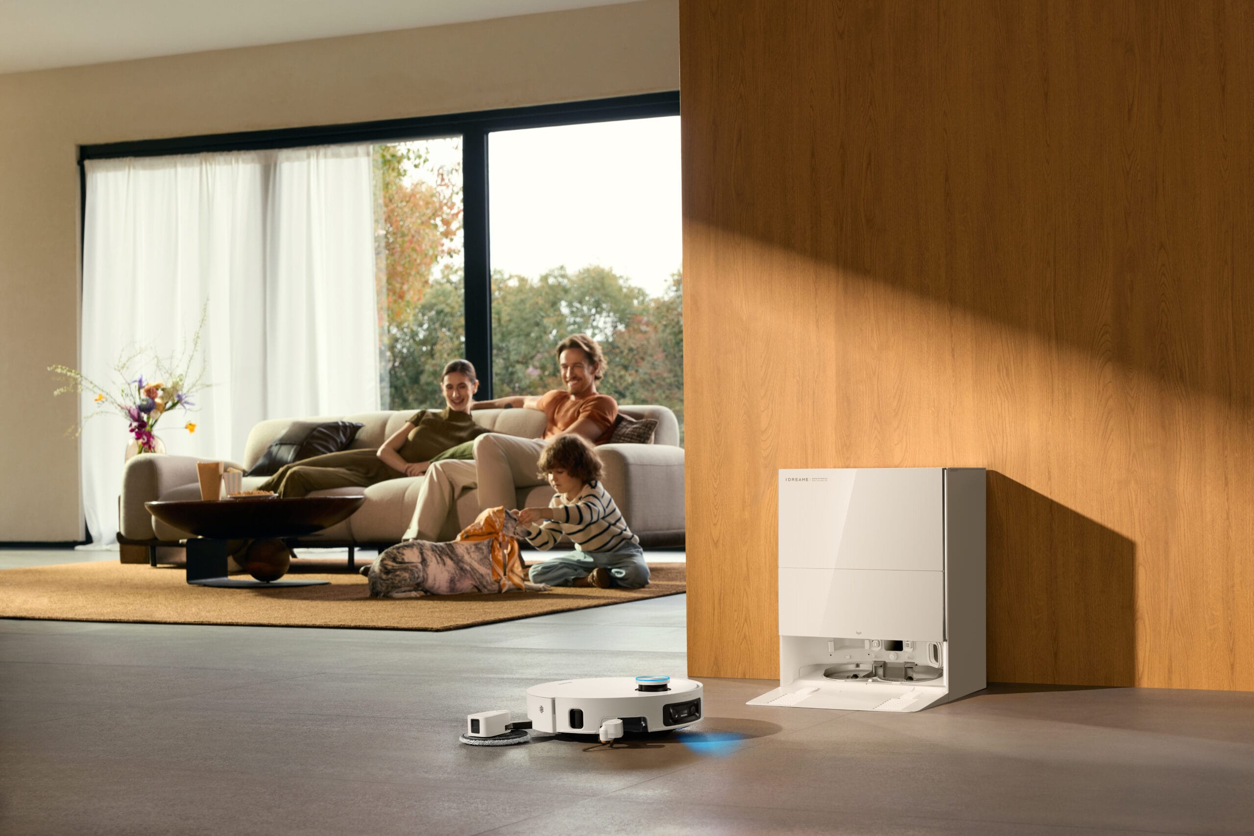 De Dreame X60 Pro Ultra robotstofzuiger rijdt weg van het basisstation in een woonkamer met een gezin op de achtergrond