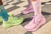 Twee lopers met roze en felgroene ASICS hardloopschoenen en bijpassende sokken op een stenen pad