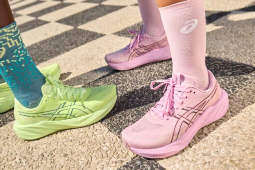 Twee lopers met roze en felgroene ASICS hardloopschoenen en bijpassende sokken op een stenen pad
