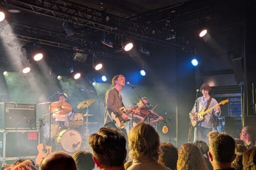 Band treedt live op met zang, viool, gitaar en drums op een verlicht podium voor een publiek
