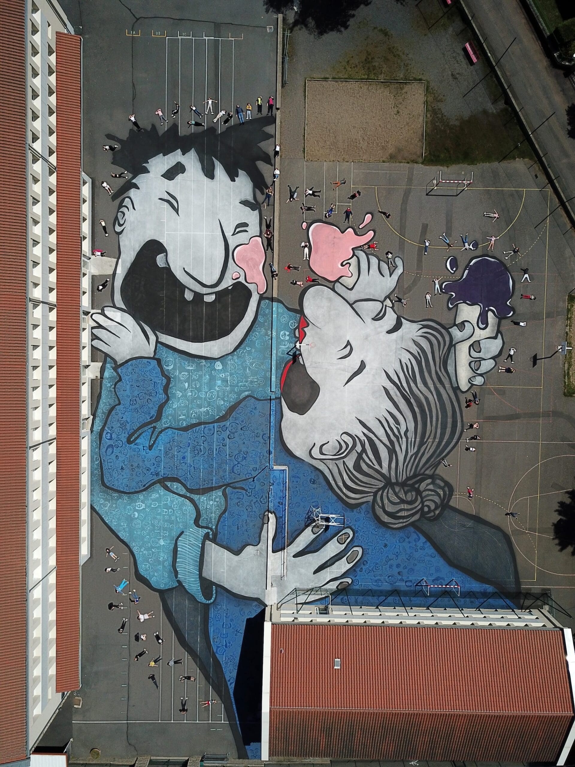 Luchtfoto van een gigantische dakschildering van twee lachende figuren die een ijsje delen op een sportveld