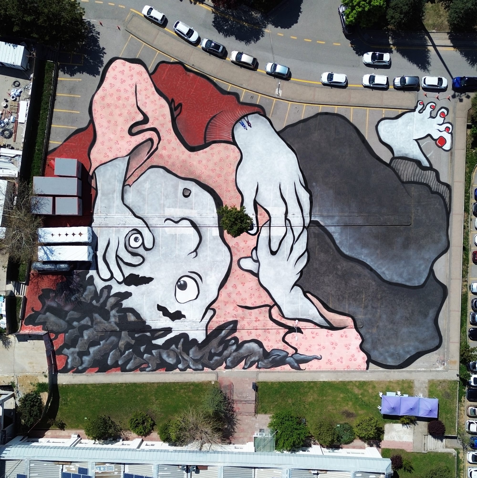 Luchtfoto van een gigantische muurschildering op een parkeerplaats van een ineengedoken figuur door Ella & Pitr