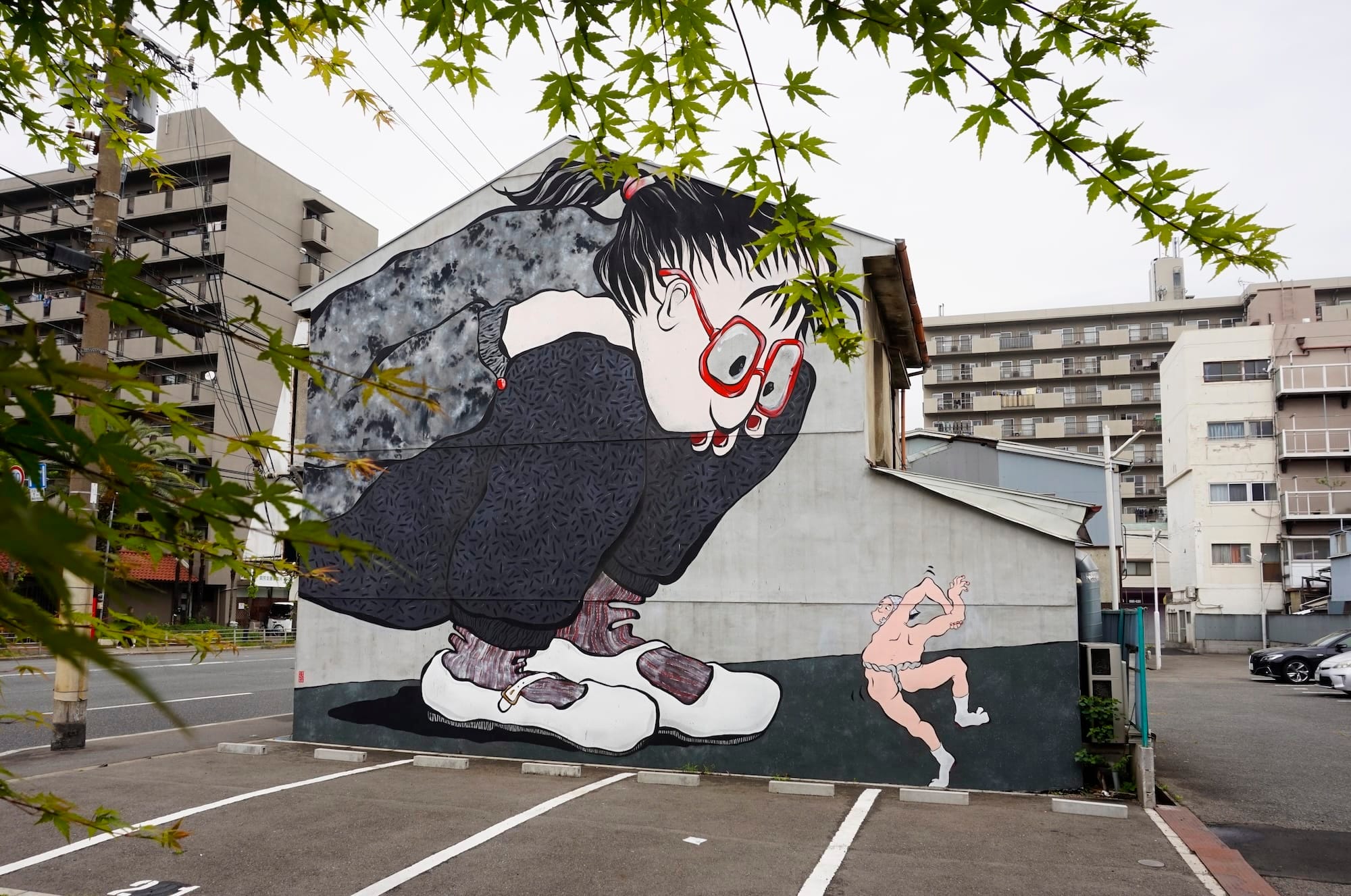 Muurschildering van een reusachtig meisje met een rode bril dat gehurkt neerkijkt op een kleine, rennende man