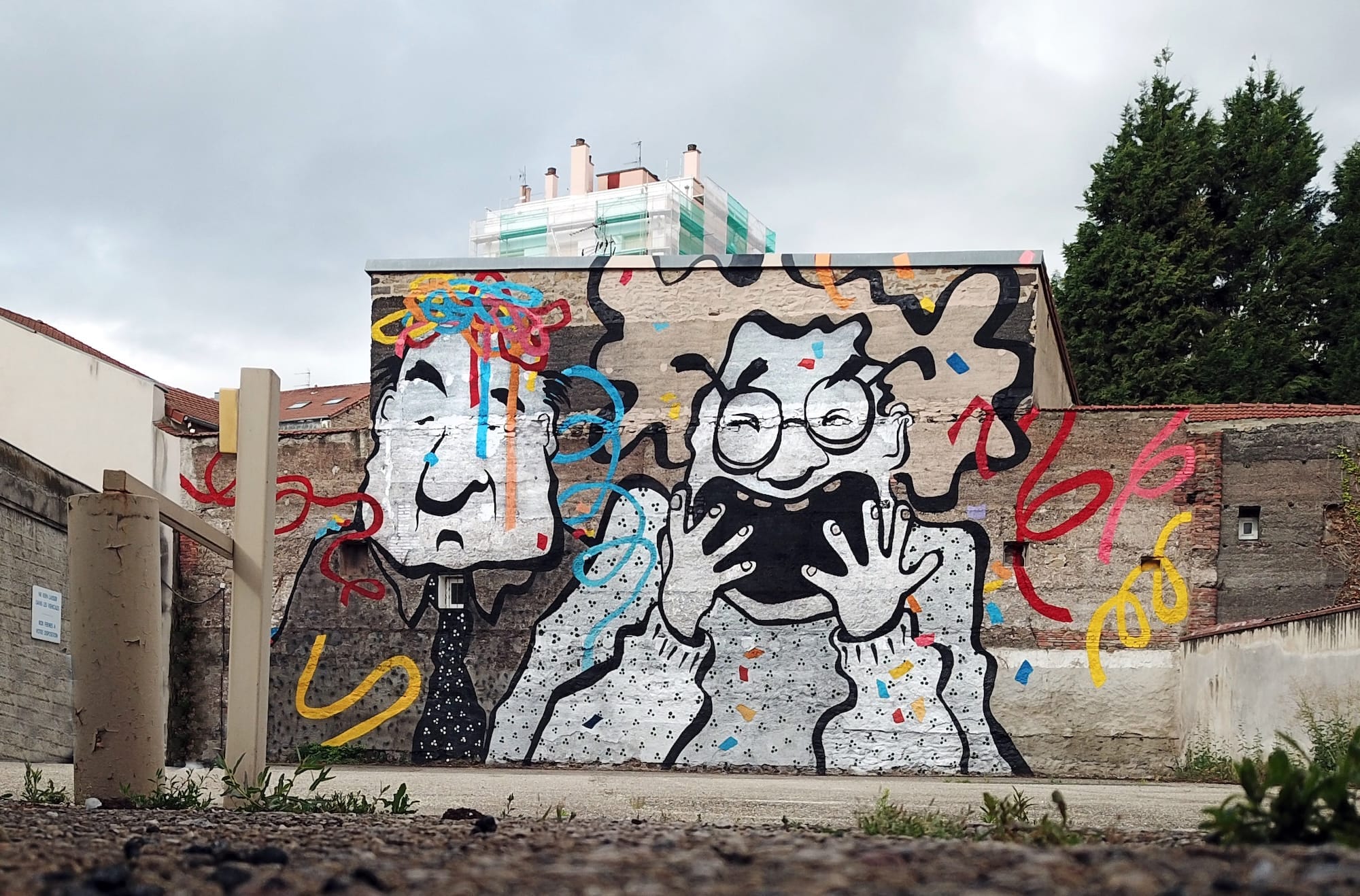 Muurschildering van twee cartooneske figuren met kleurrijke krabbels op een grijze stenen stadsmuur