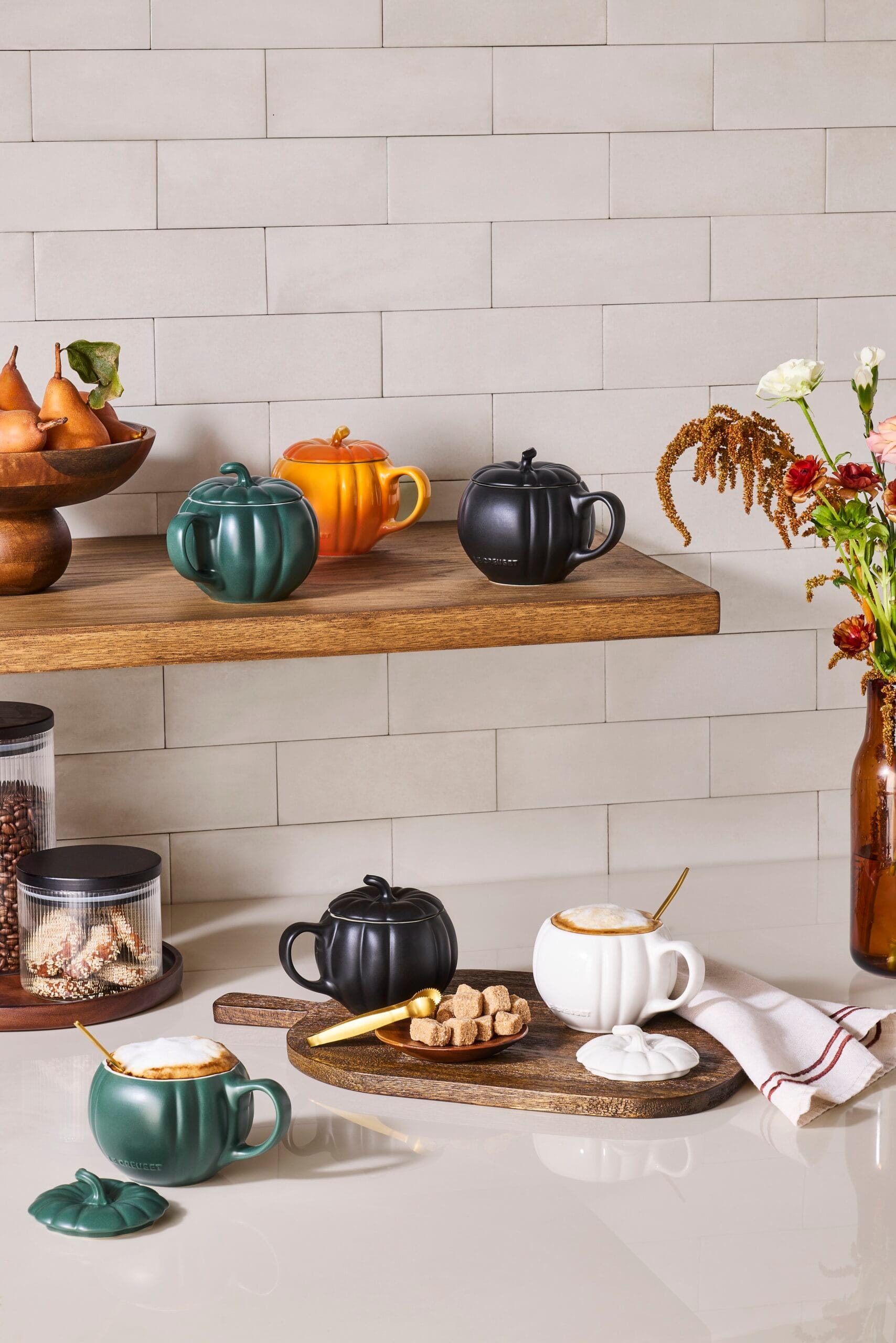 Pompoenvormige mokken met deksel van Le Creuset in verschillende kleuren op een keukenplank en aanrecht