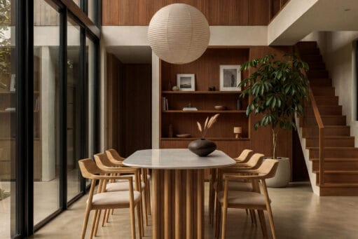 Modern minimalistische eetkamer met een op maat gemaakte tafel van Table du Sud bestaande uit houten poten en een keramisch blad , verder zijn er een witte bolvormige hanglamp, hoge ramen en houten wandbekleding