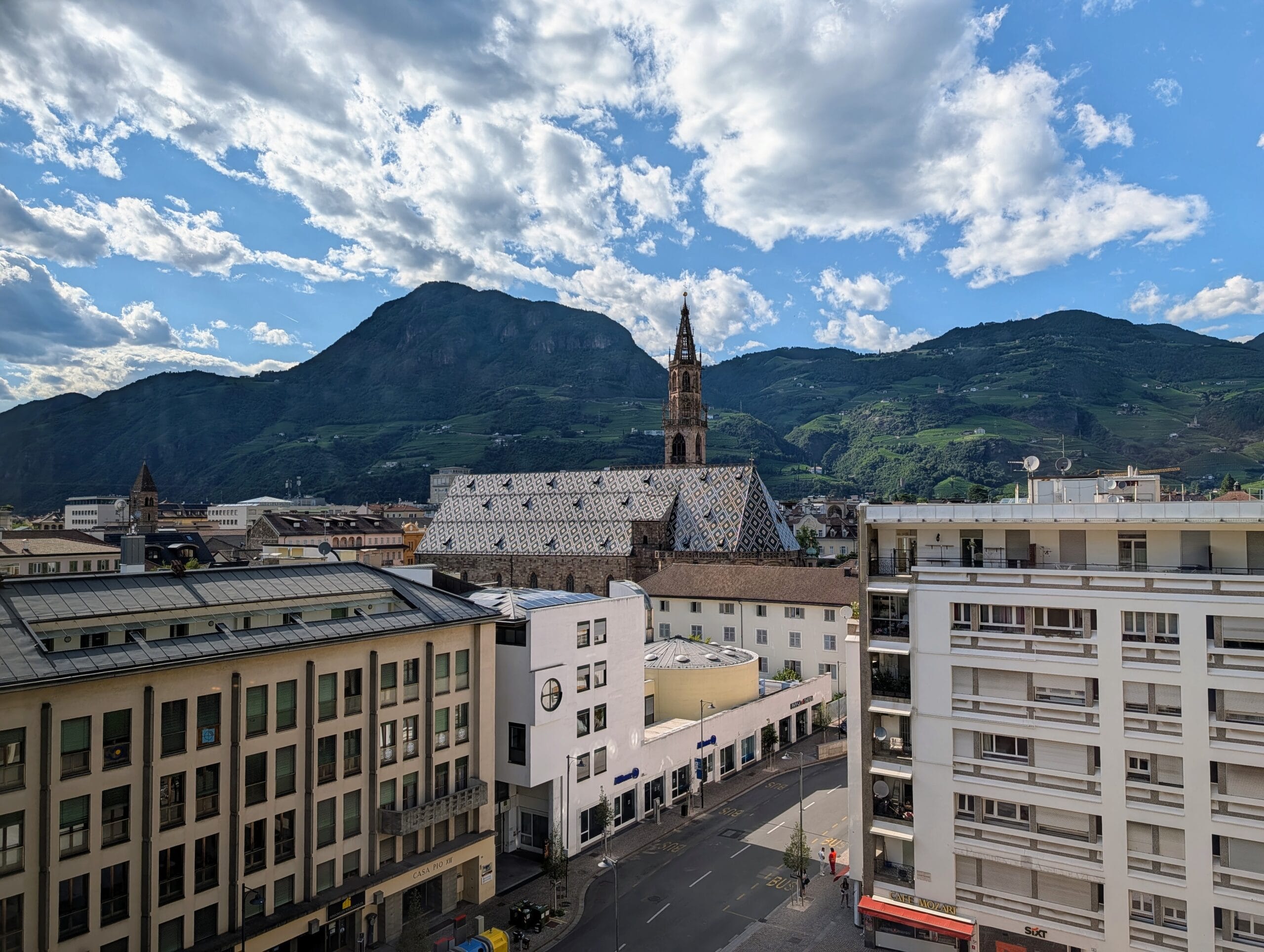 Zicht op de daken van Bolzano, de kathedraal met patroondak en de omringende bergen