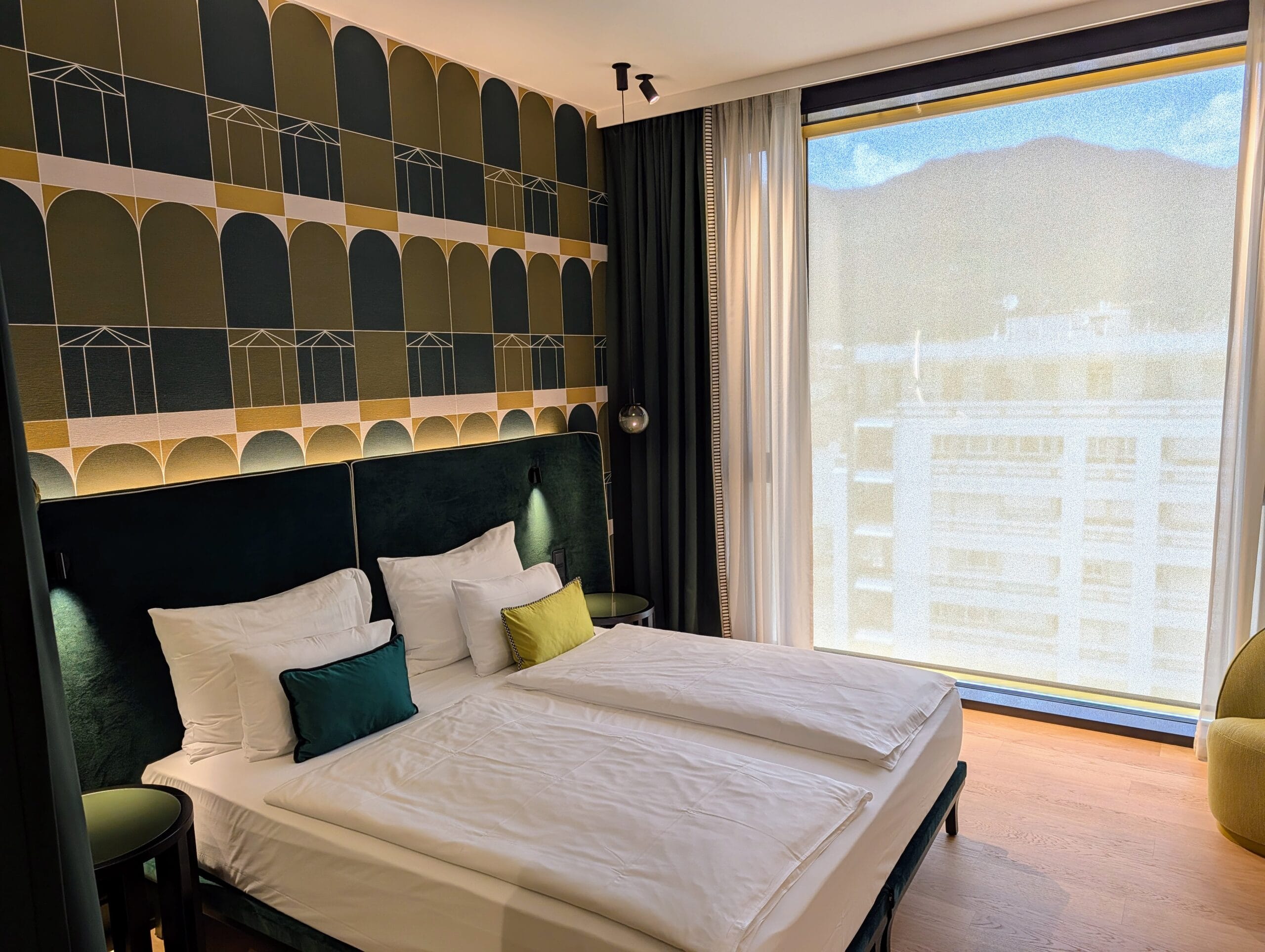 Luxe hotelkamer in Falkensteiner Hotel Bozen met een tweepersoonsbed, groen grafisch behang en uitzicht door een groot raam