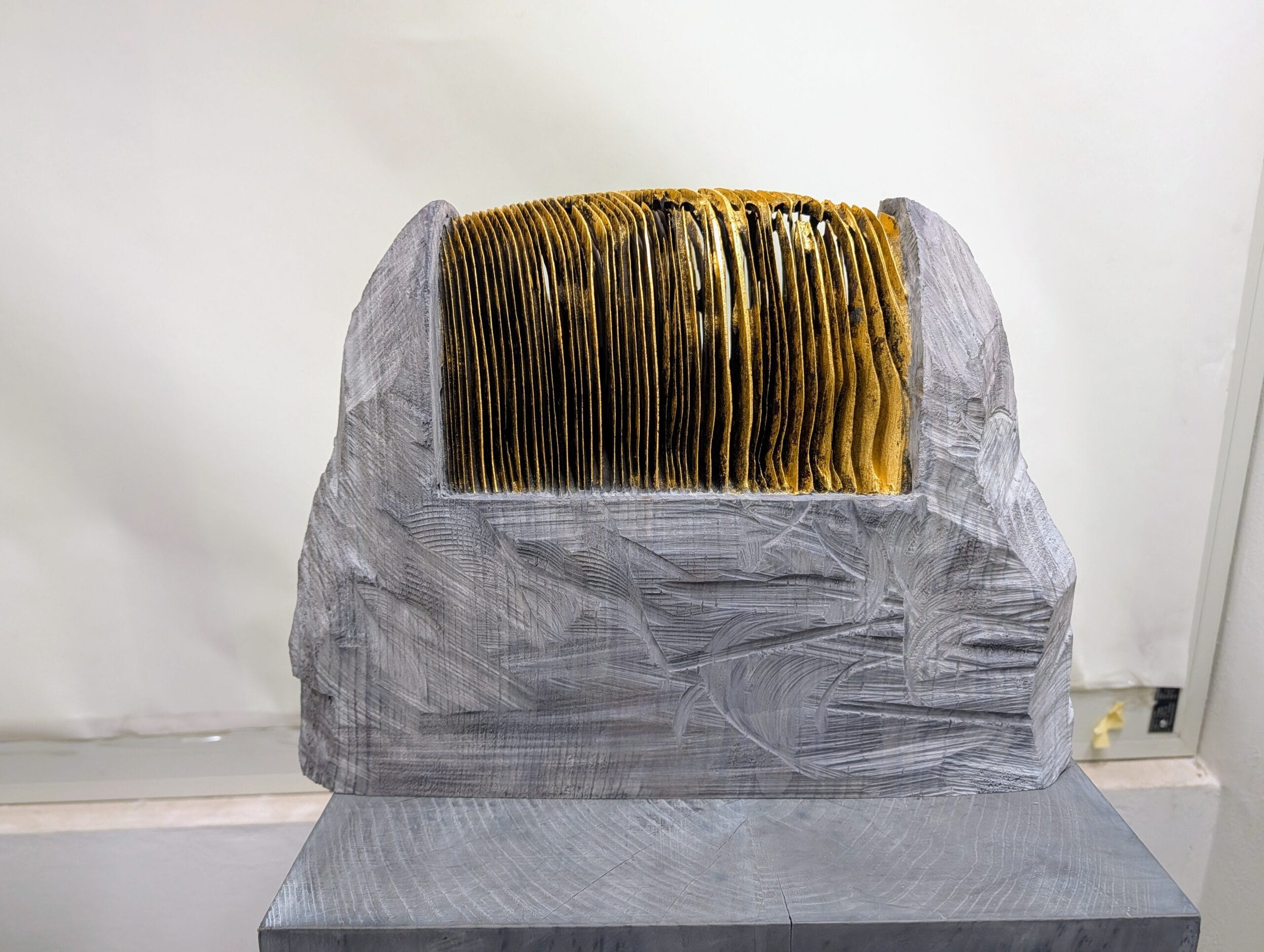 Houten sculptuur van kunstenaar Aron Demetz met fijne gouden lamellen in een grijs bewerkt blok