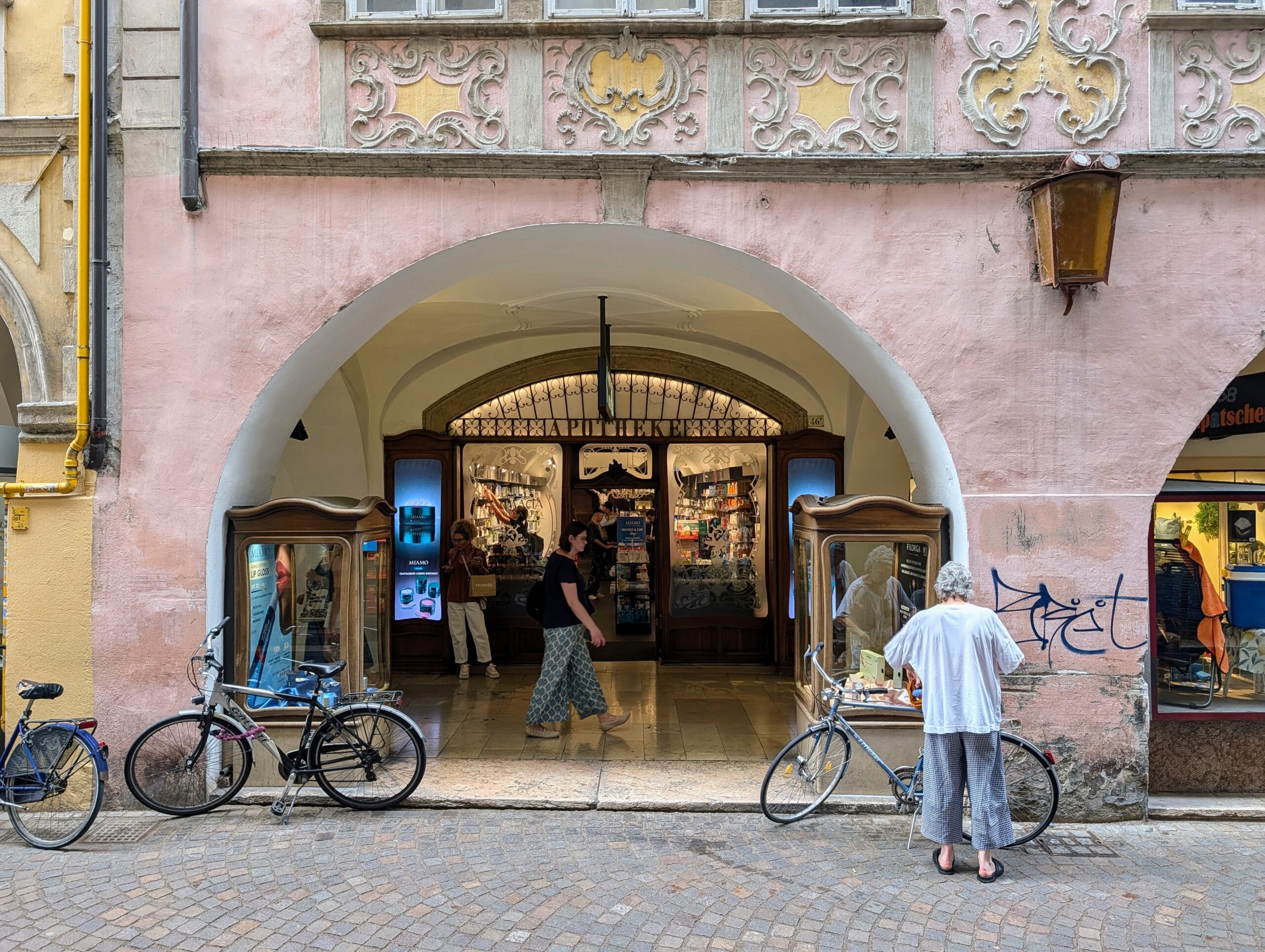 Historische apotheek onder een boog in een roze gevel met sierstucwerk en geparkeerde fietsen
