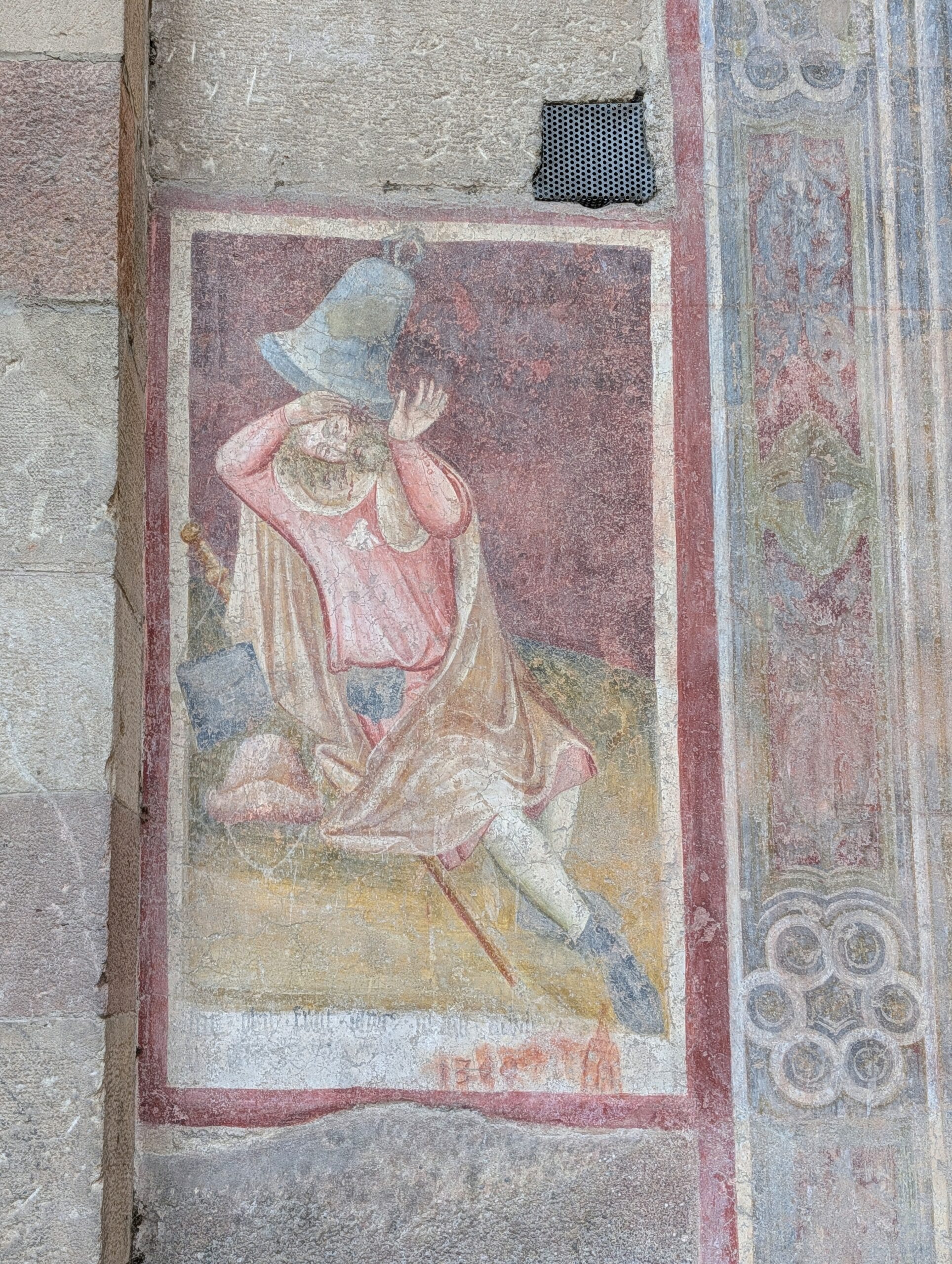 Historisch fresco op een stenen muur van een zittende figuur met een grote luidklok over het hoofd