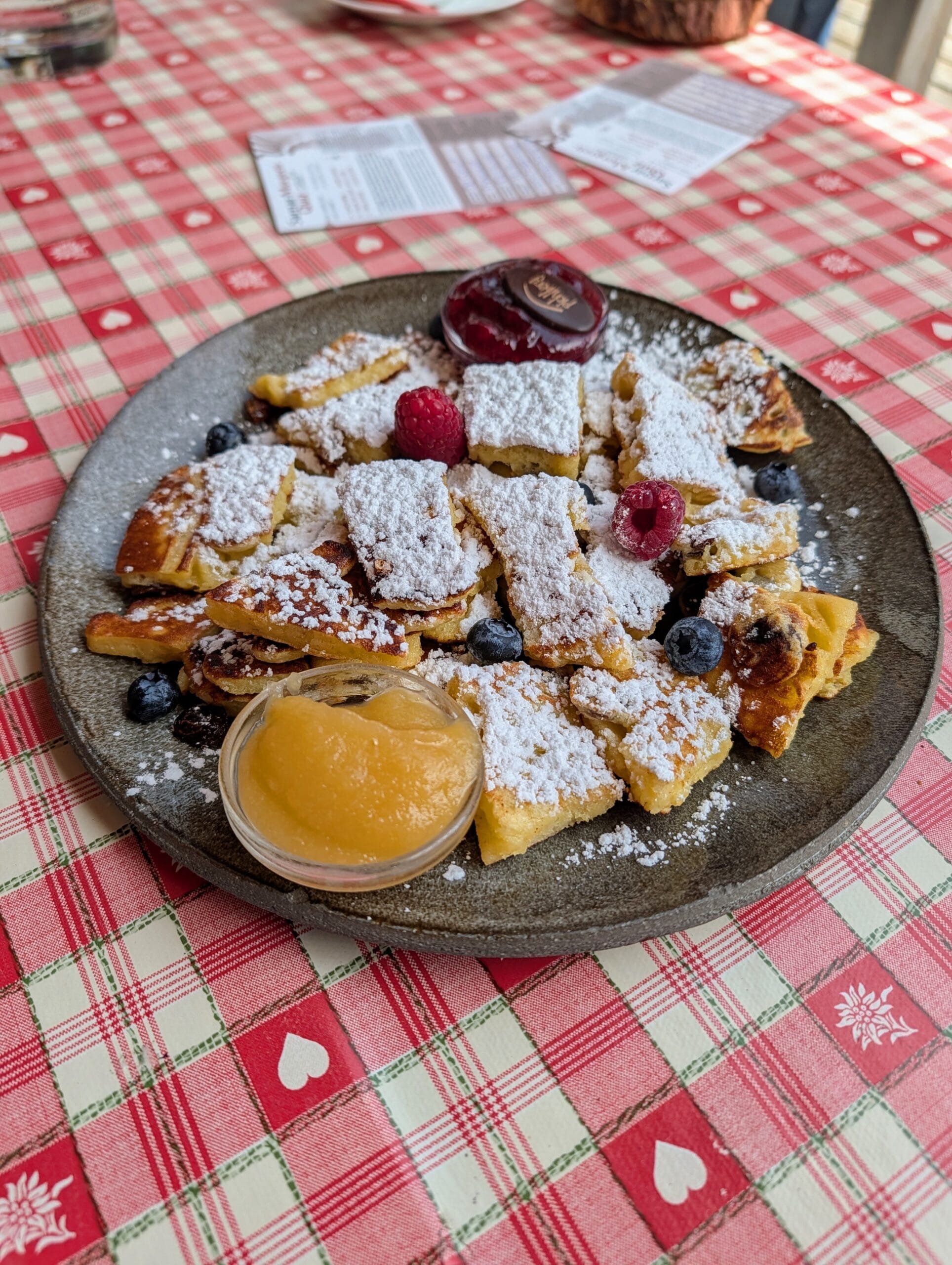 Bord met Kaiserschmarrn bestrooid met poedersuiker, geserveerd met appelmoes, rode bessenjam en vers fruit