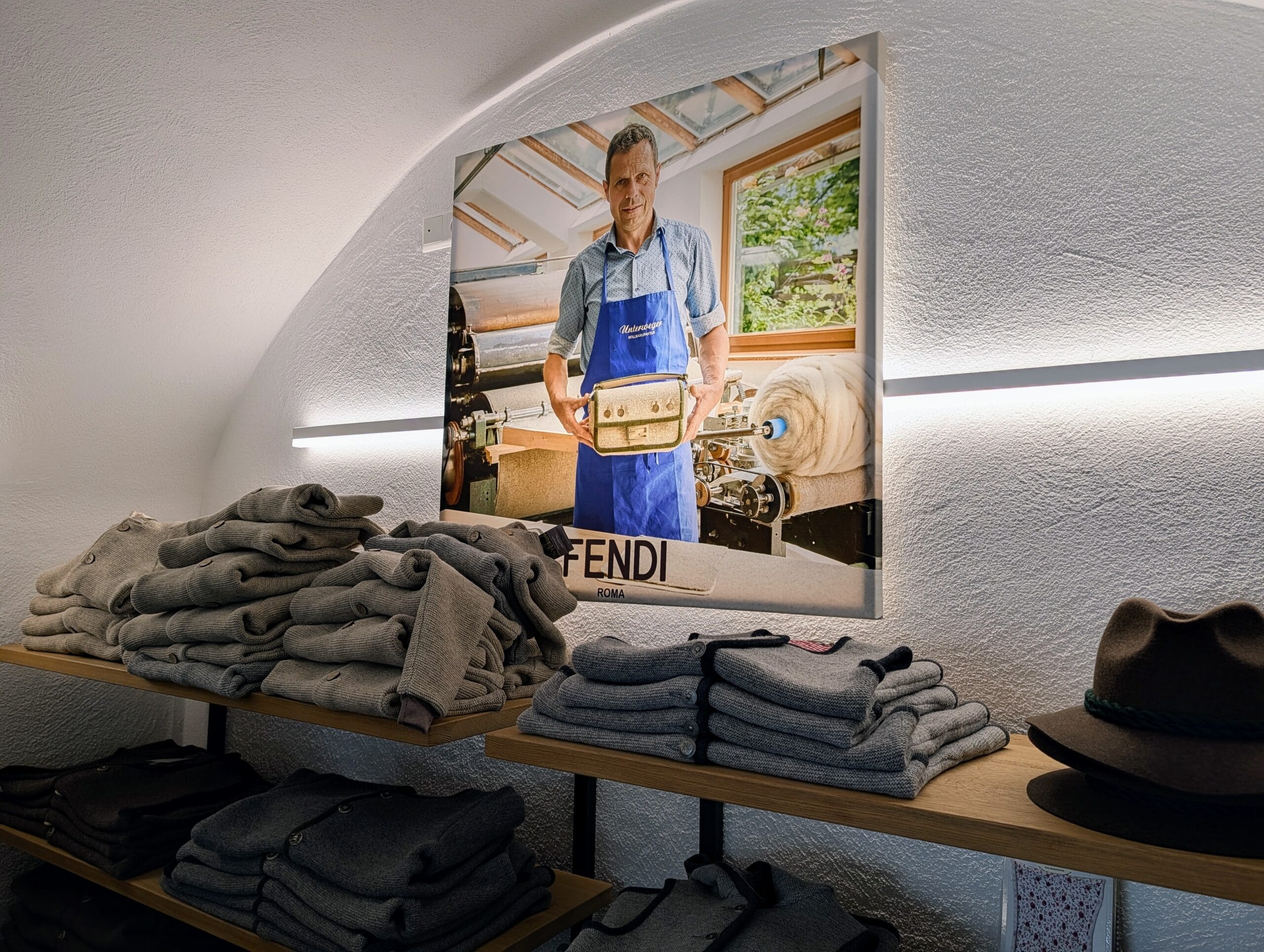 Wollen kleding in de winkel van Wollmanufaktur Unterweger, met een foto van Albert Unterweger en de Fendi-tas