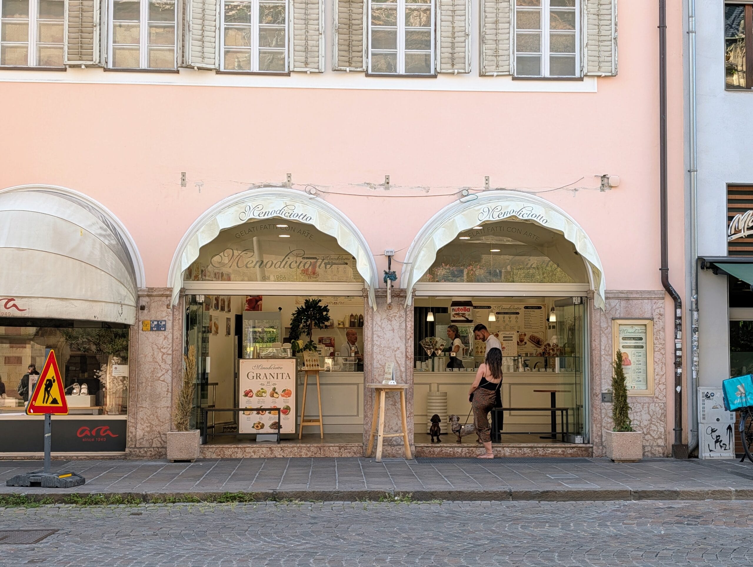 De voorgevel van ijssalon Menodiciotto in een roze gebouw in Bolzano, met klanten bij de toonbank