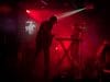 Muzikanten treden live op een podium op onder fel rood licht en rook, met een toetsenist en gitarist