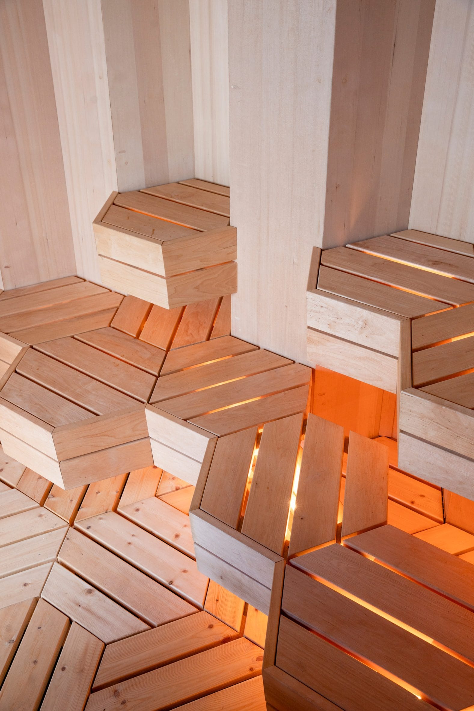 Interieur van de sauna met geometrische, zeshoekige houten banken die van binnenuit warm oranje verlicht zijn