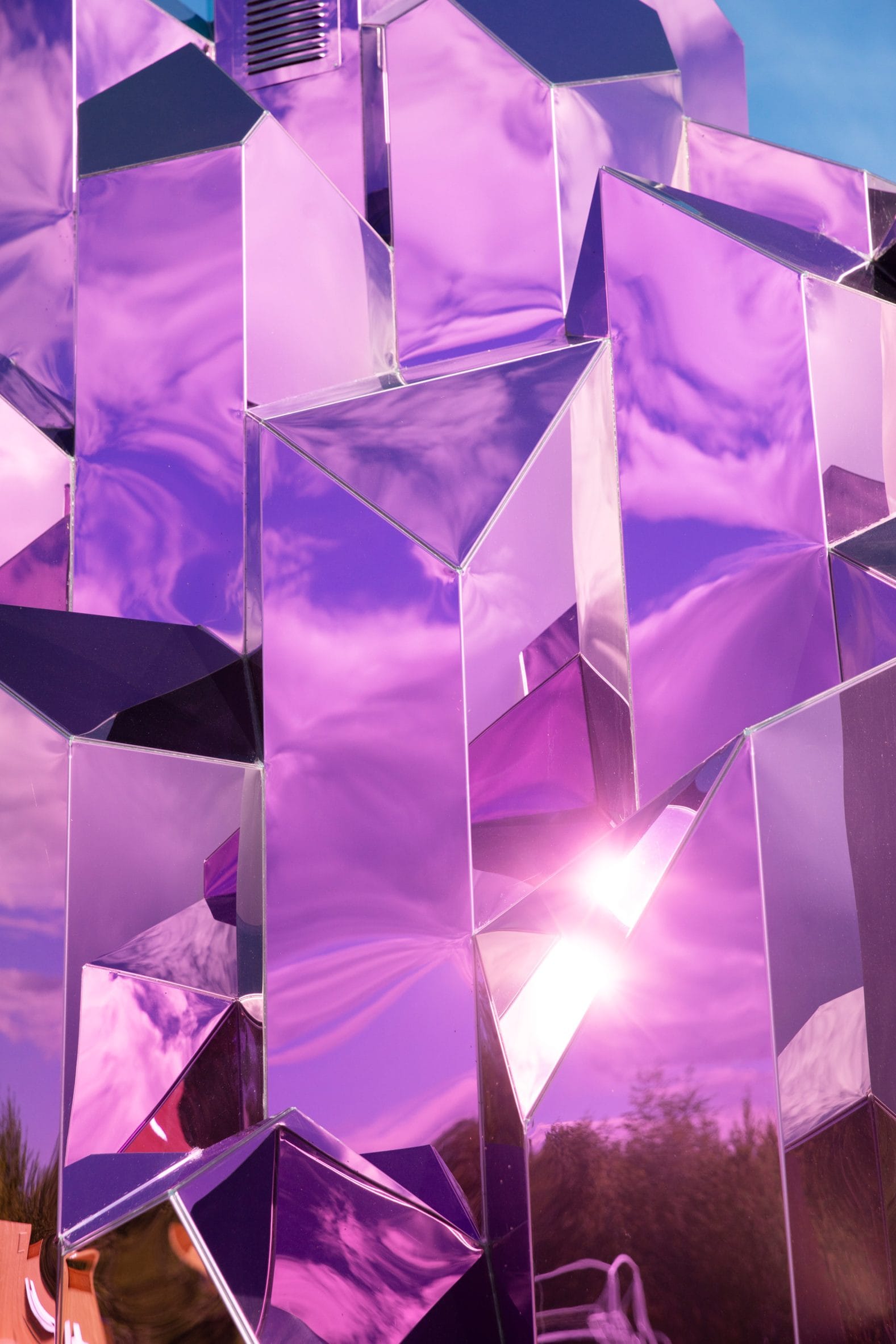 Detail van de Lithium Crystal Sauna bestaande uit hoekige, roze spiegelende panelen die de lucht en omgeving reflecteren