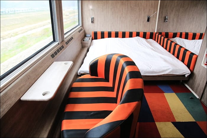 Interieur van een slaapcabine in de Rail Cruise Haerang met een bed, gestreepte bank en uitzicht door het raam