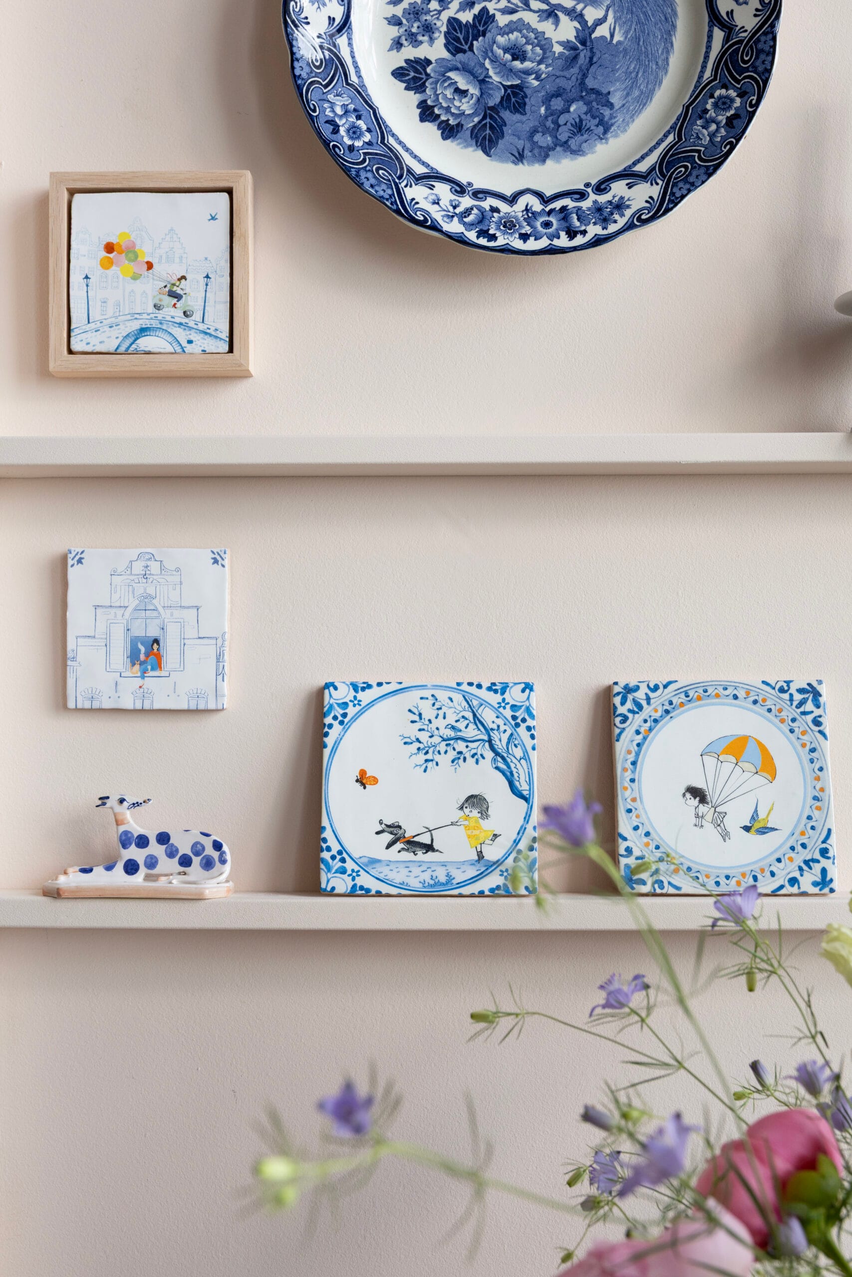Wandplanken gedecoreerd met moderne Delfts blauwe tegeltjes, een keramieken bord met bloemen en een dierenfiguurtje, Uit de collectie van StoryTiles x Fiep Westendorp