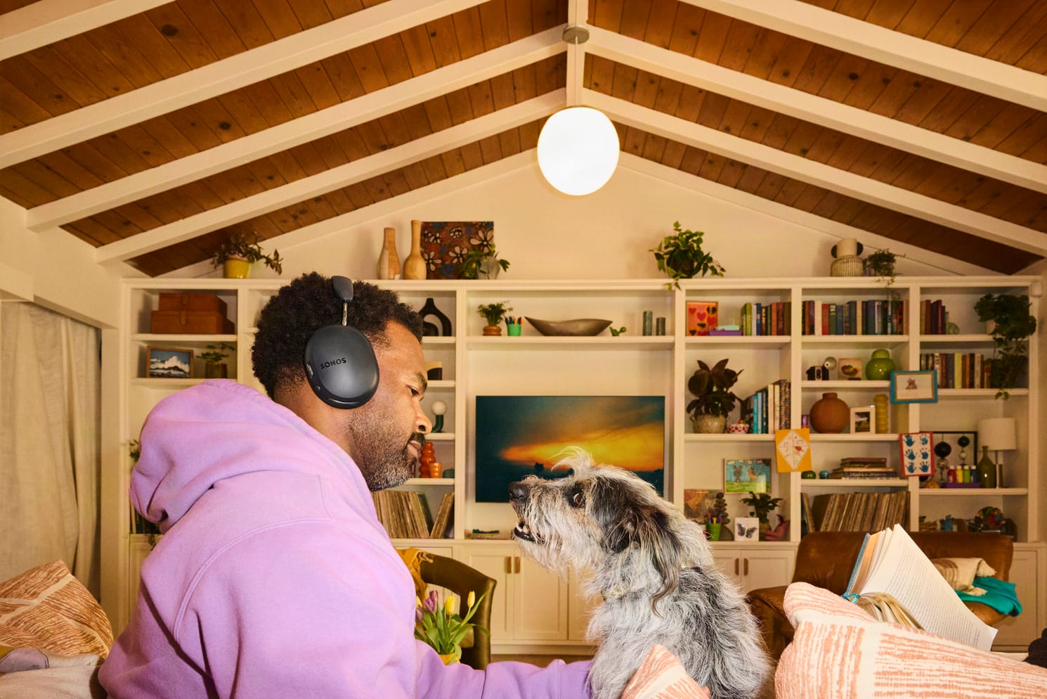 Man met zwarte Sonos Ace Ultra-koptelefoon kijkt naar zijn hond in de woonkamer
