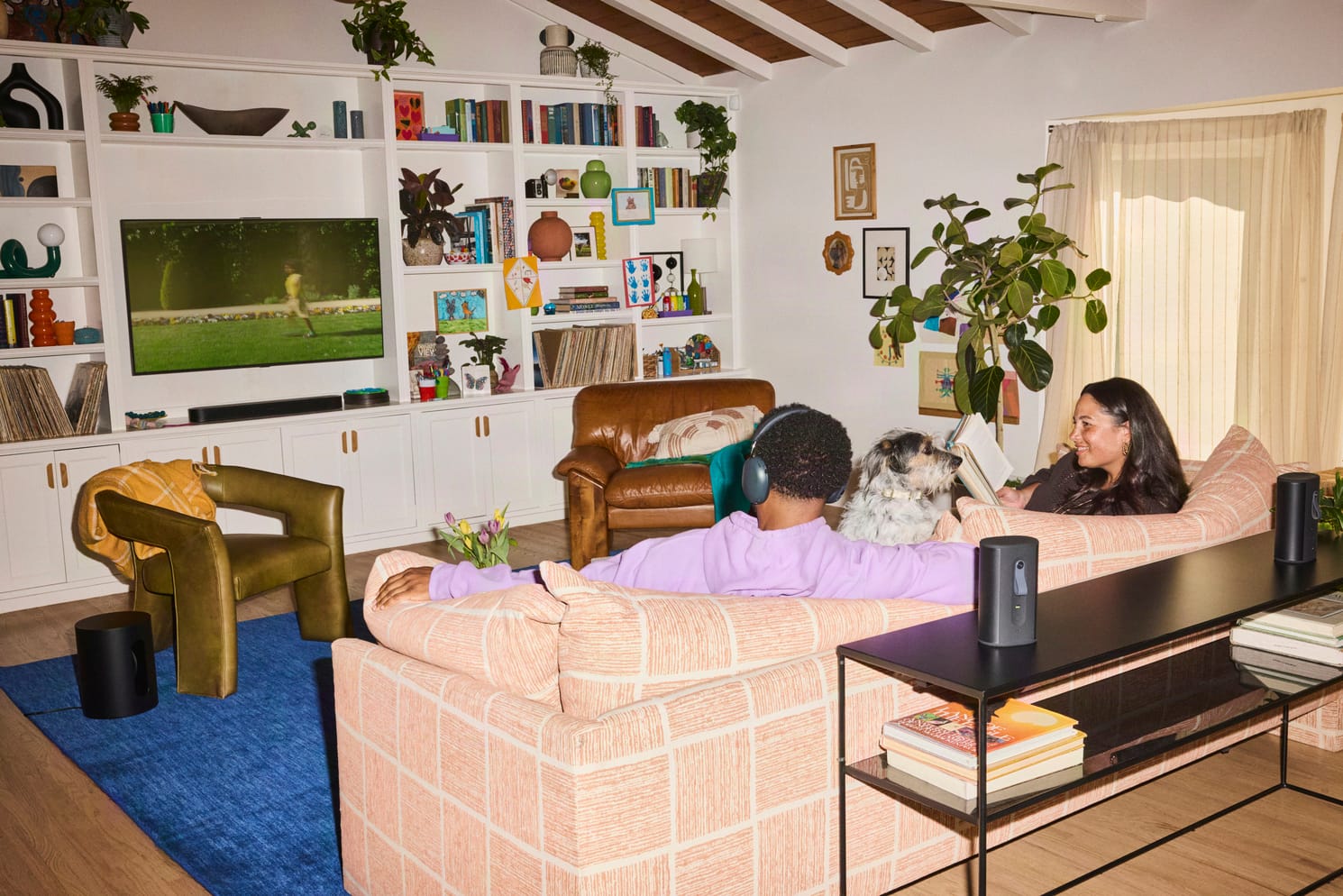 Woonkamer met een Sonos-soundbar onder de tv, een man met een Sonos-koptelefoon op de bank en surroundspeakers erachter