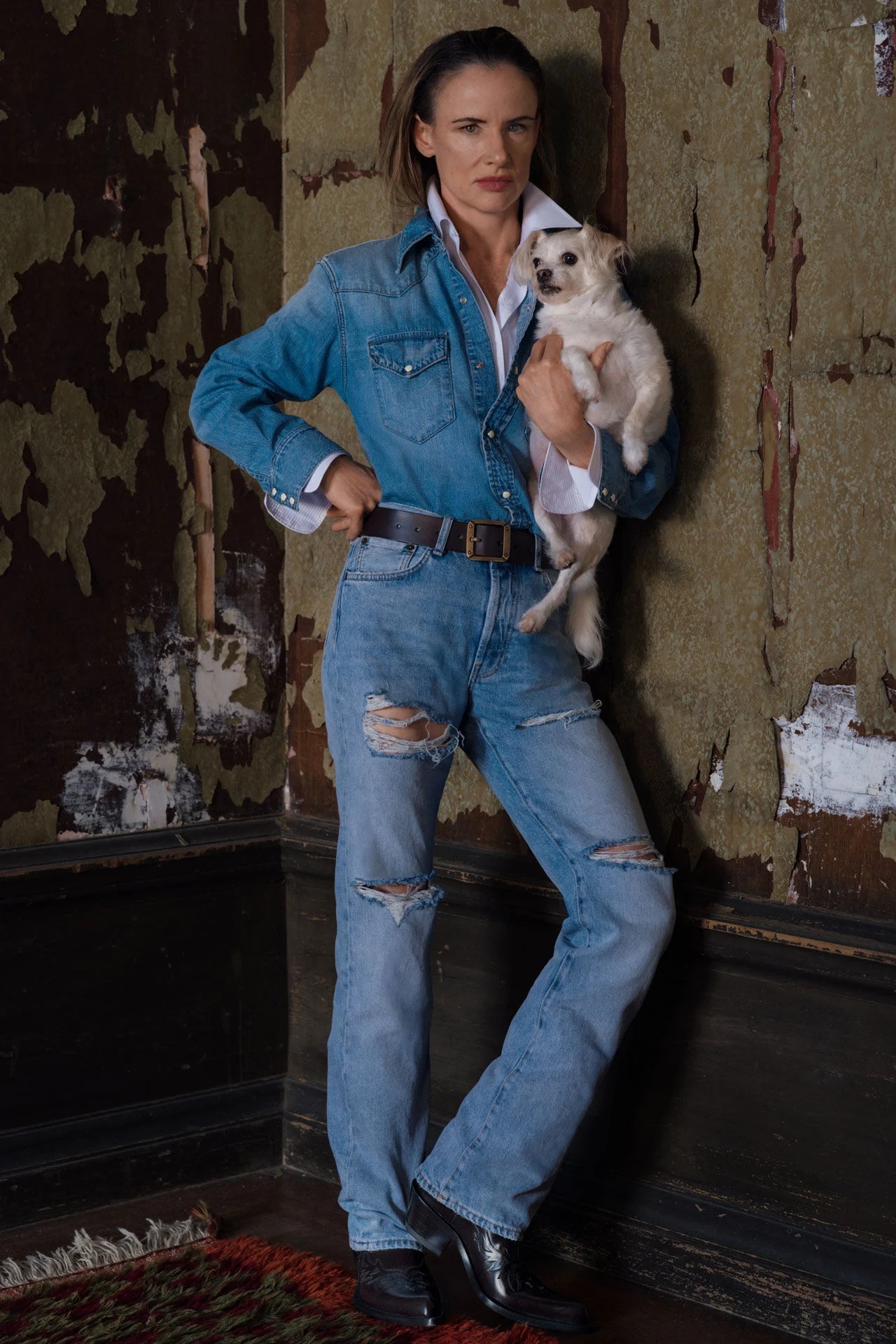 Staand in een spijkeroverhemd en gescheurde jeans met een klein wit hondje in haar armen