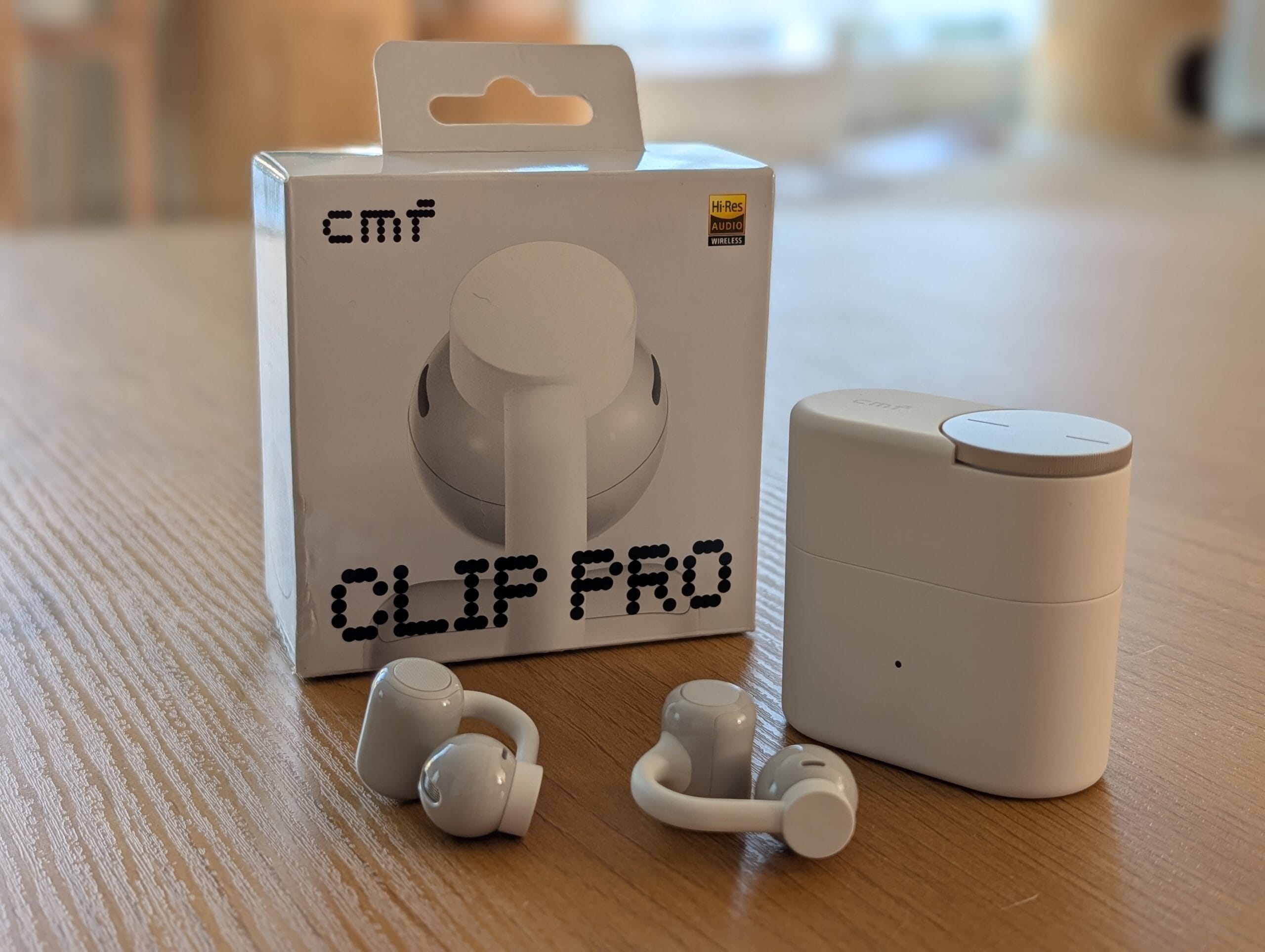 De CMF Clip Pro oordopjes naast de bijbehorende oplaadcase en verpakking op een houten tafel