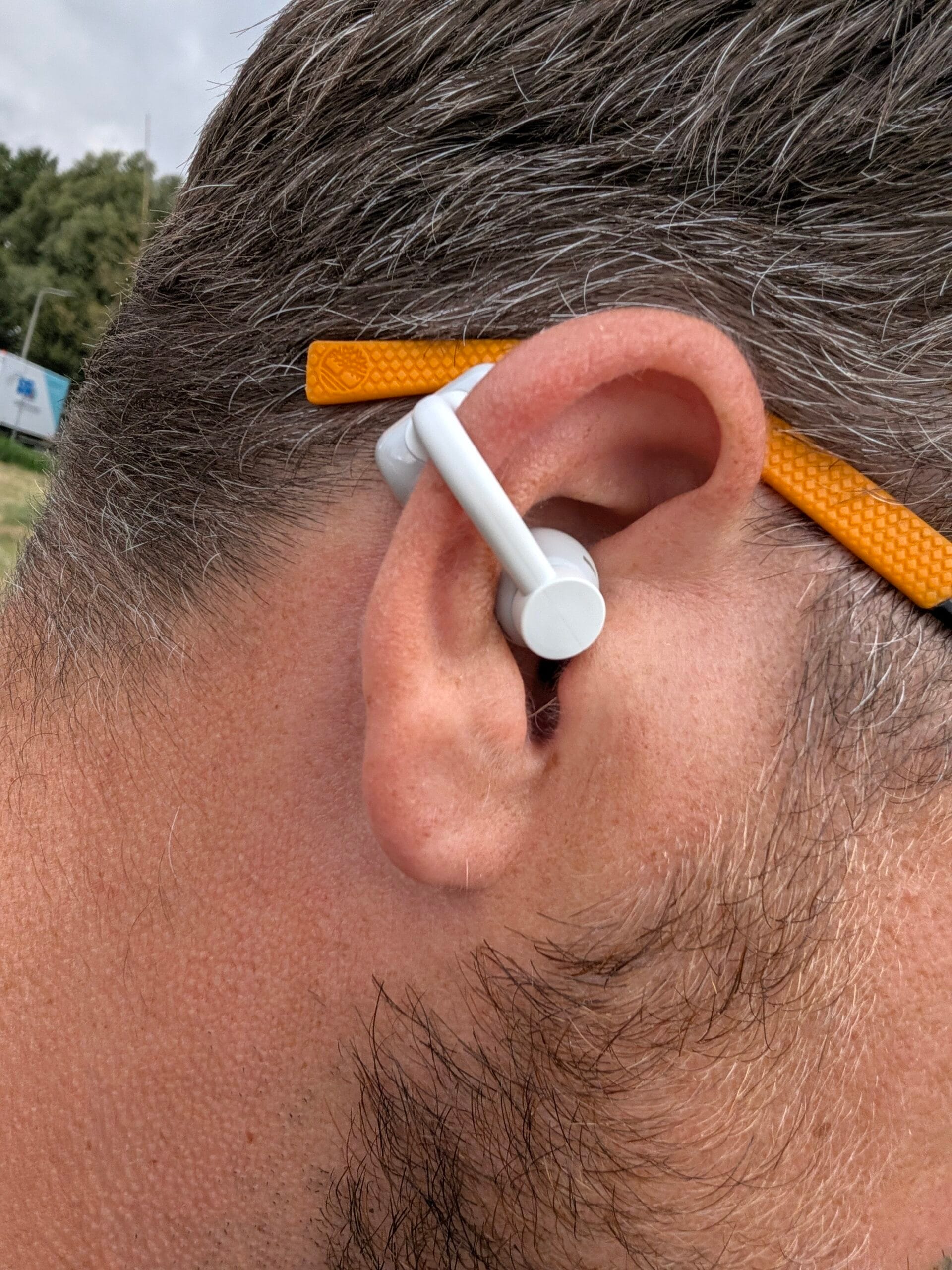 Witte CMF Clip Pro gedragen op een oor, gecombineerd met een bril met oranje montuur