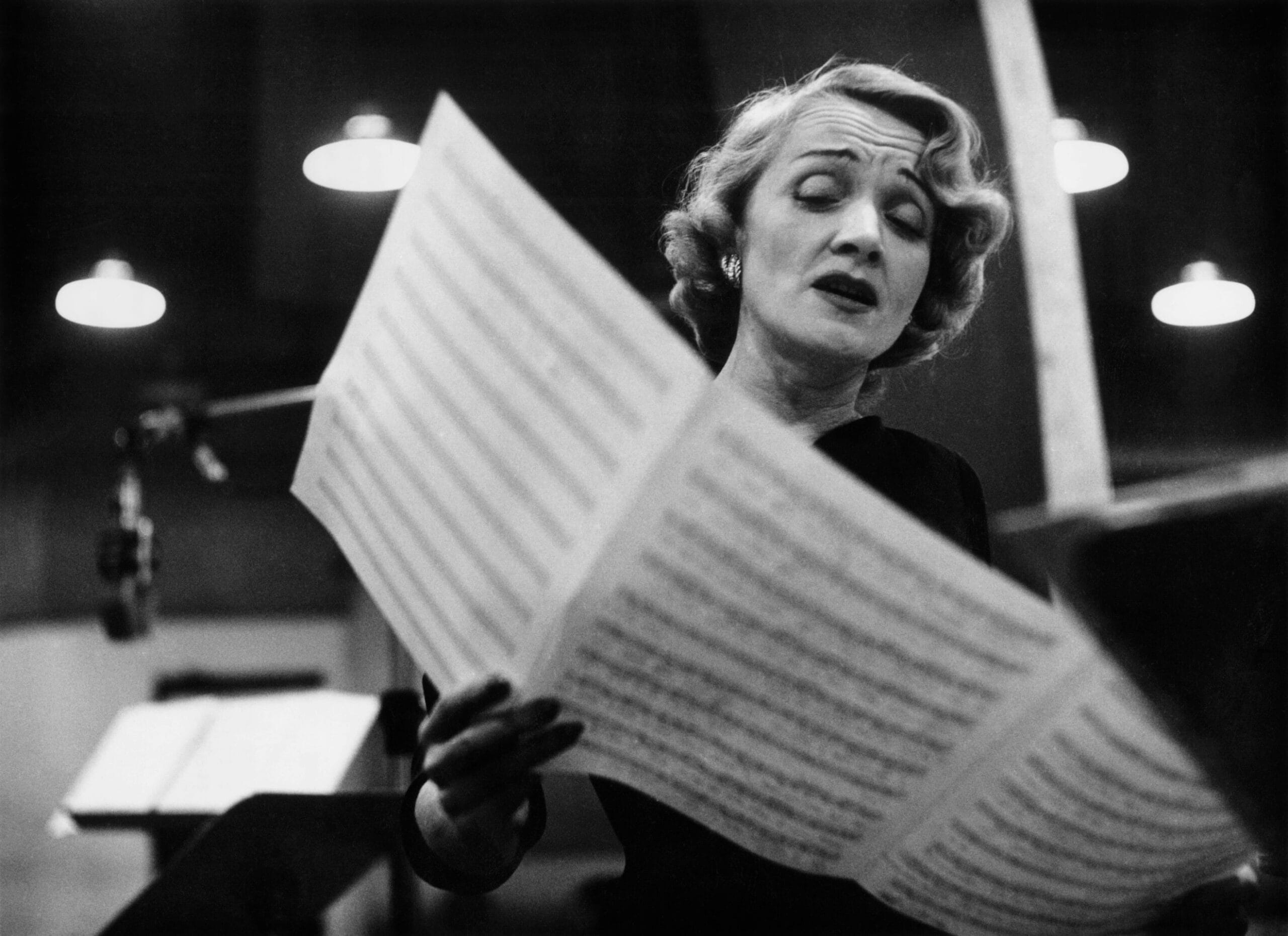Marlene Dietrich zingt met gesloten ogen in een opnamestudio terwijl ze bladmuziek vasthoudt, gefotografeerd door Eve Arnold in 1952