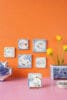 Geïllustreerde Delfts blauwe tegeltjes aan een oranje muur met een vaas gele tulpen en een Delfts blauw spaarvarken, ter promotie van de collectie StoryTiles x Fiep Westendorp