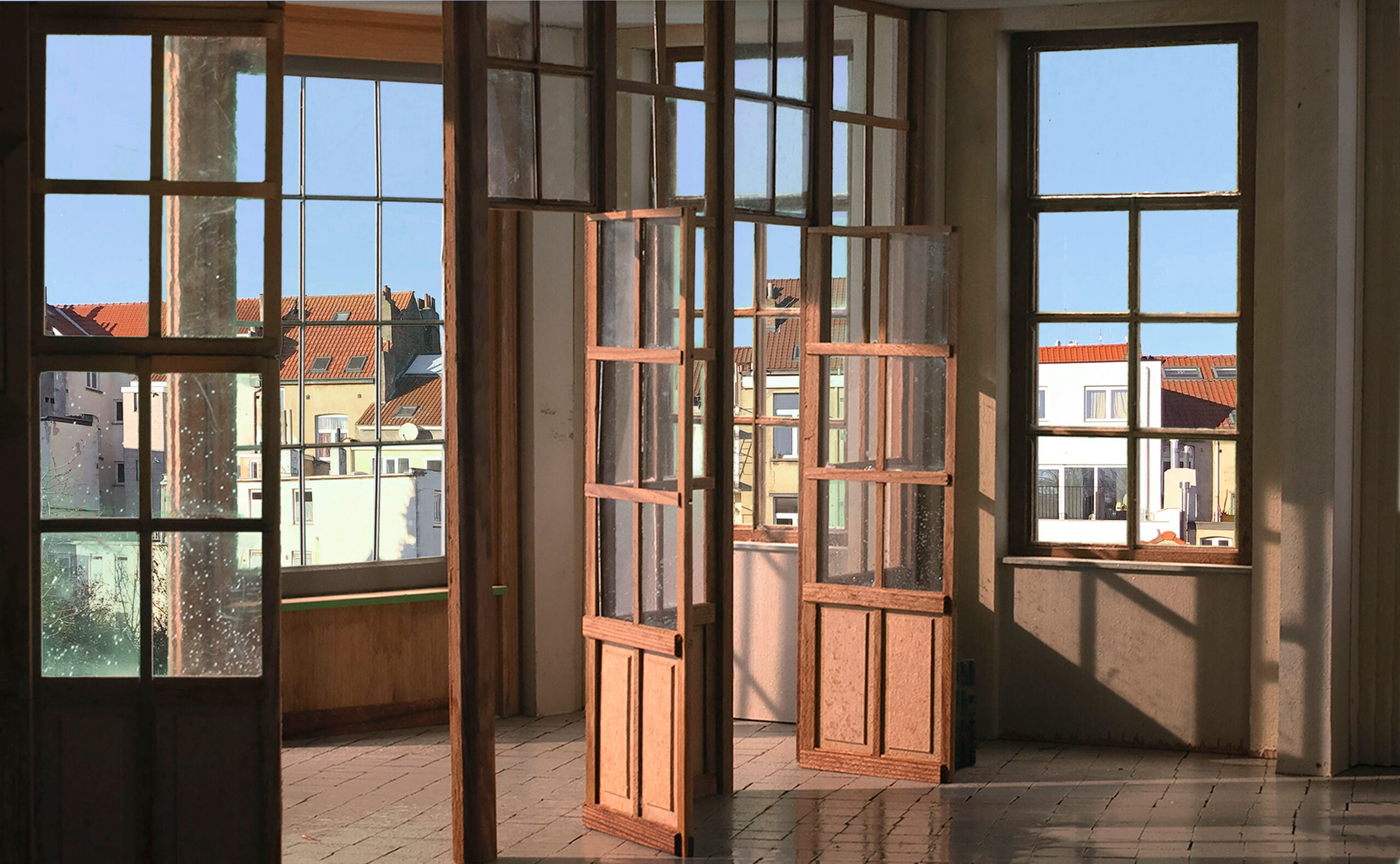Lichtovergoten interieur met houten raamdeuren die uitkijken op Brusselse daken en achtergevels