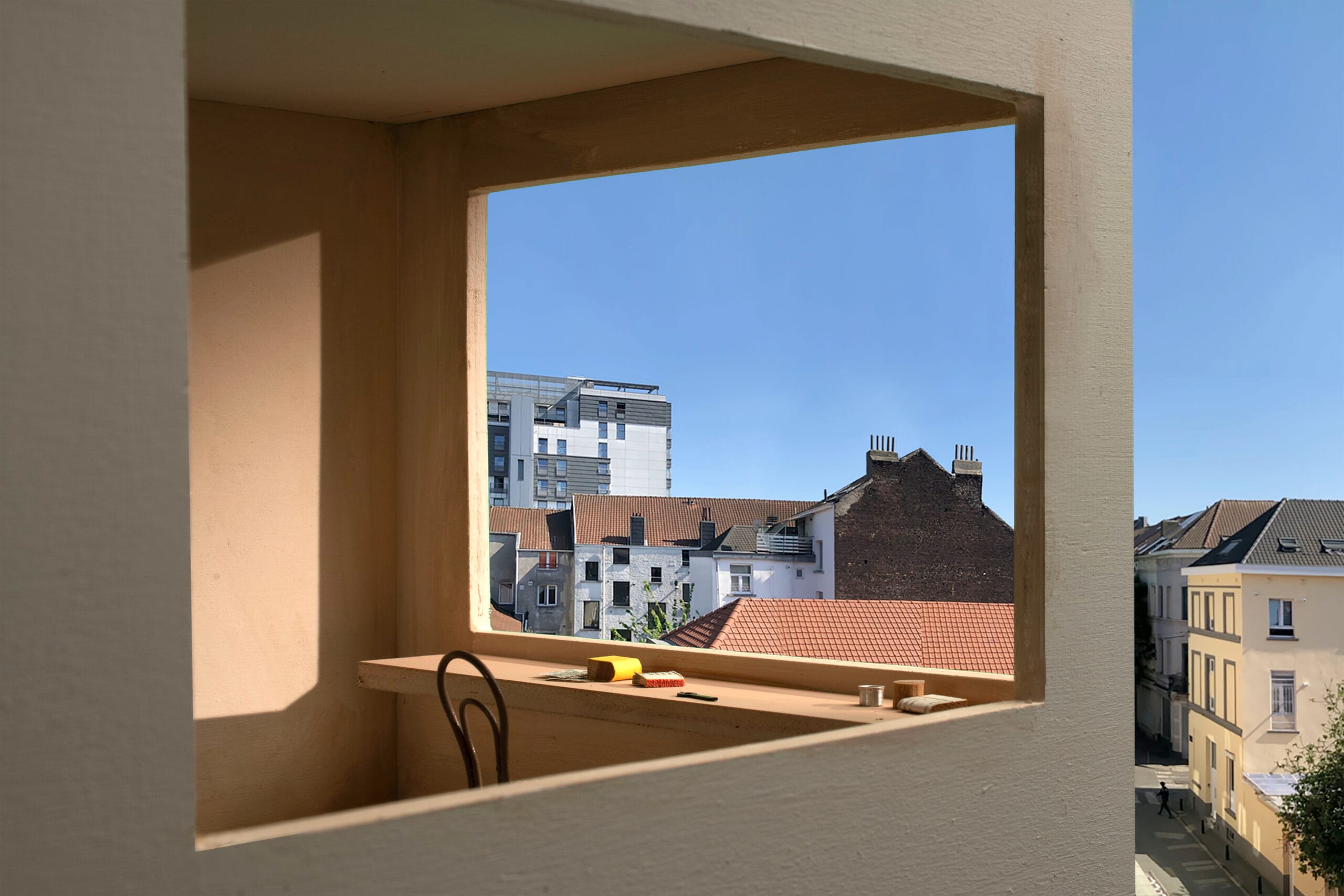 Uitzicht door het raamkozijn van een maquette op Brusselse daken en gebouwen onder een blauwe hemel