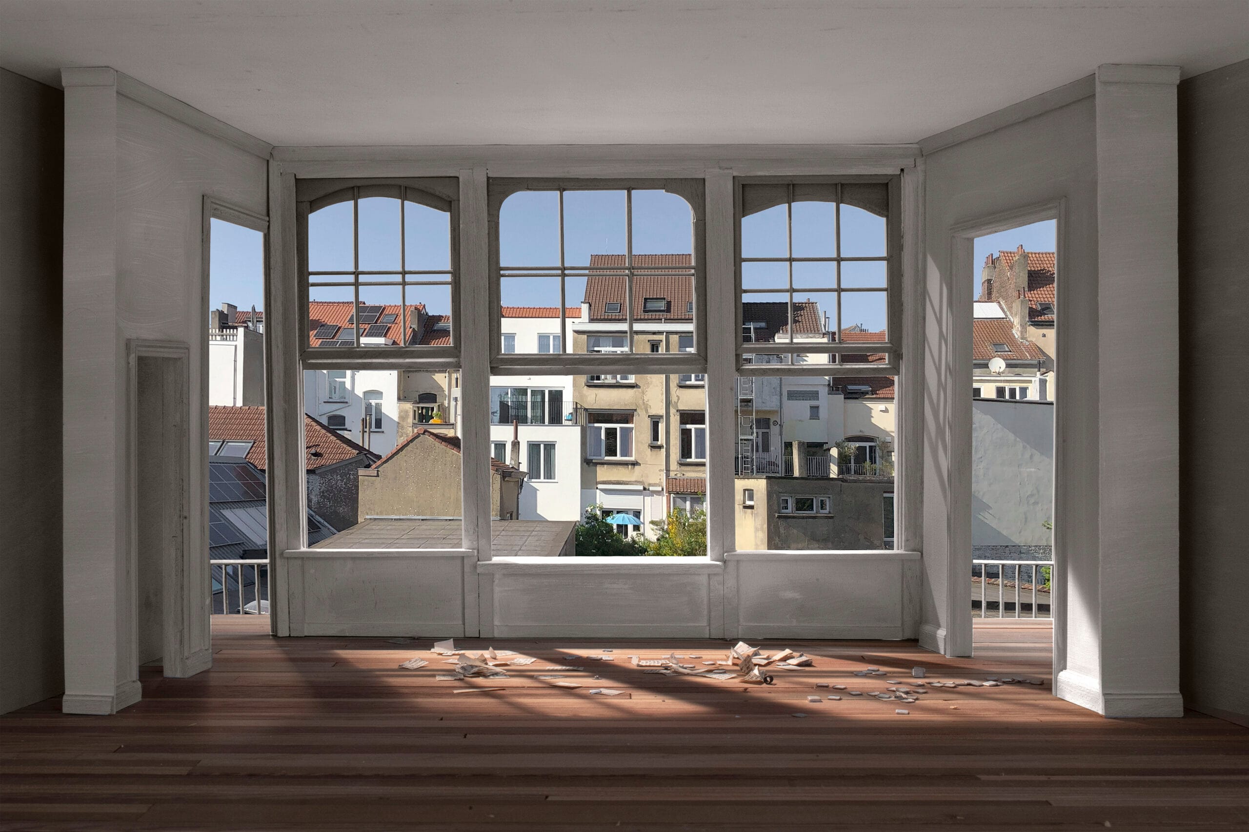 Maquette van een lege kamer met houten vloer en uitzicht door grote ramen op Brusselse achtergevels