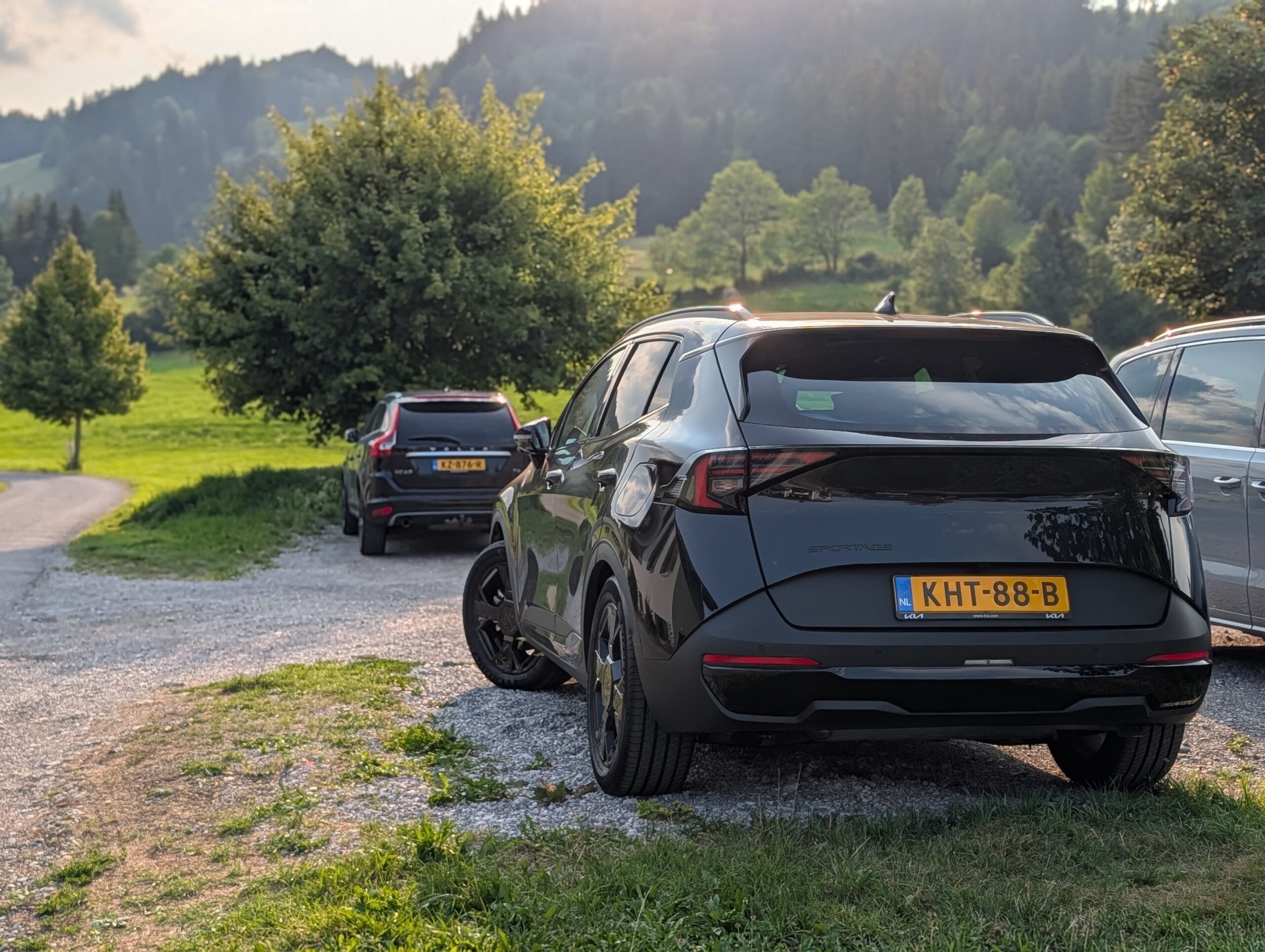 Achterzijde van een zwarte Kia Sportage geparkeerd op een grindpad in een bergachtig groen landschap