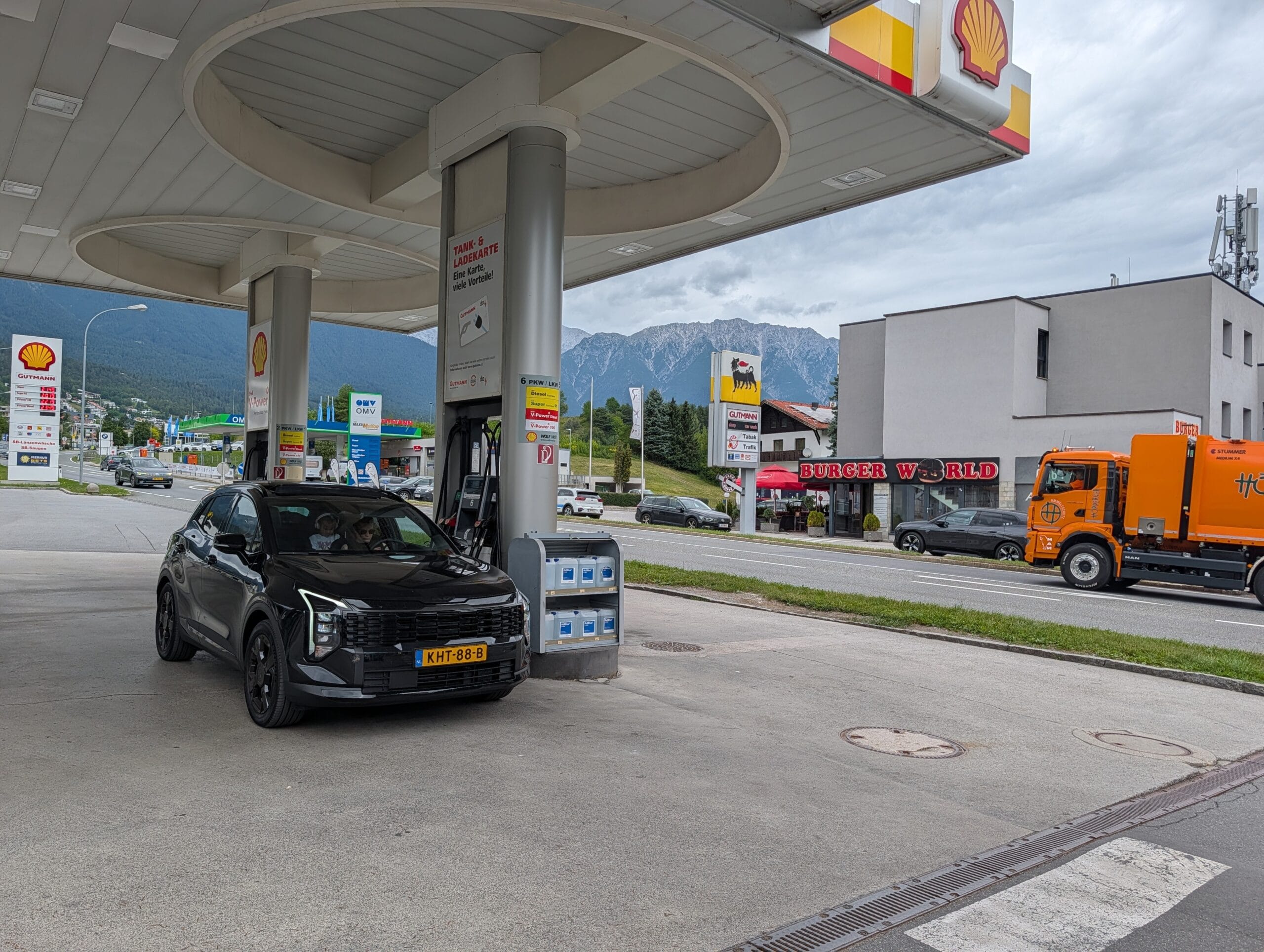 De zwarte Kia Sportage staat geparkeerd bij een Shell-tankstation met de Alpen op de achtergrond