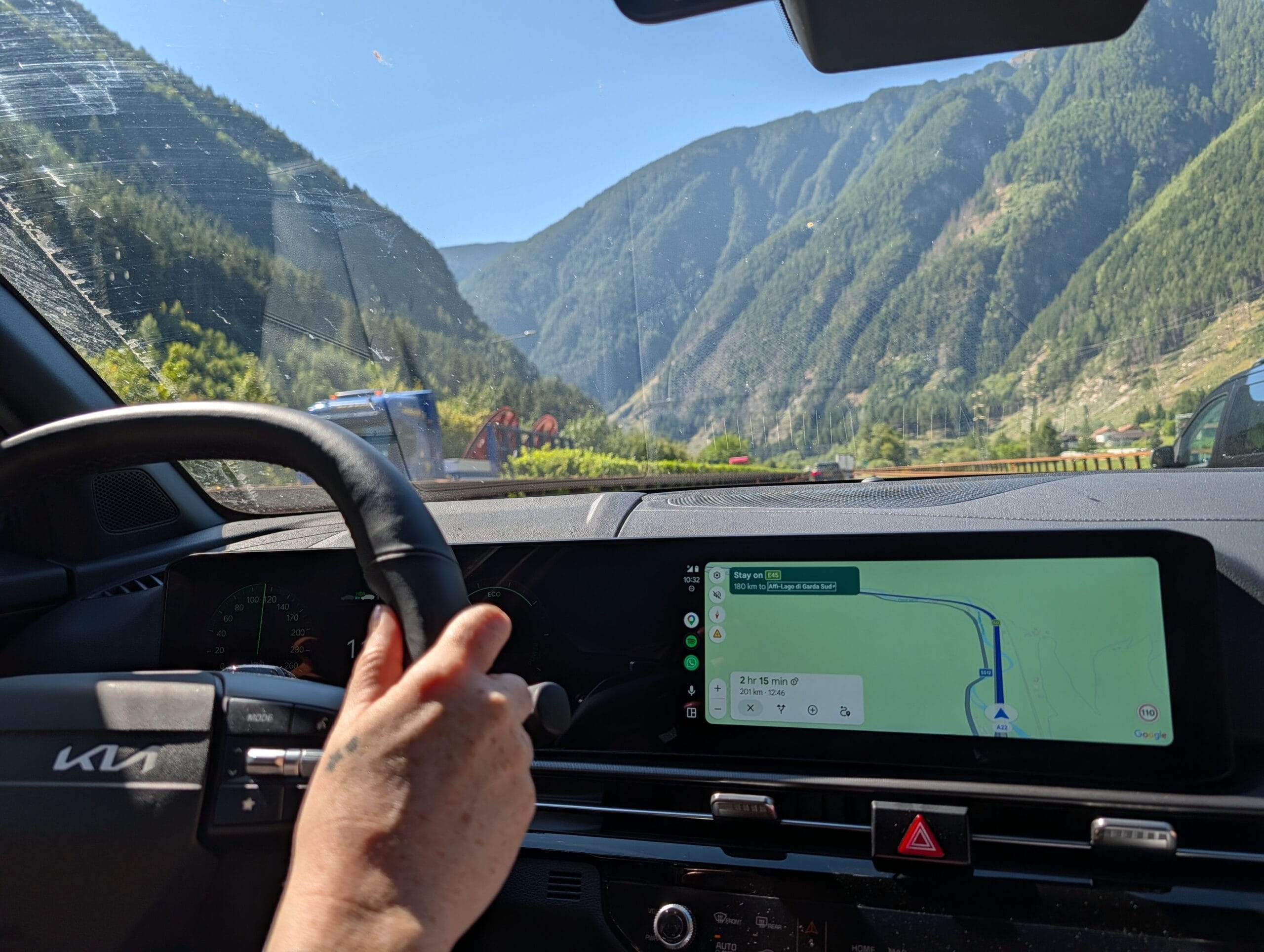 Bestuurder achter het stuur van de Kia Sportage met navigatie via het scherm, rijdend langs een berglandschap