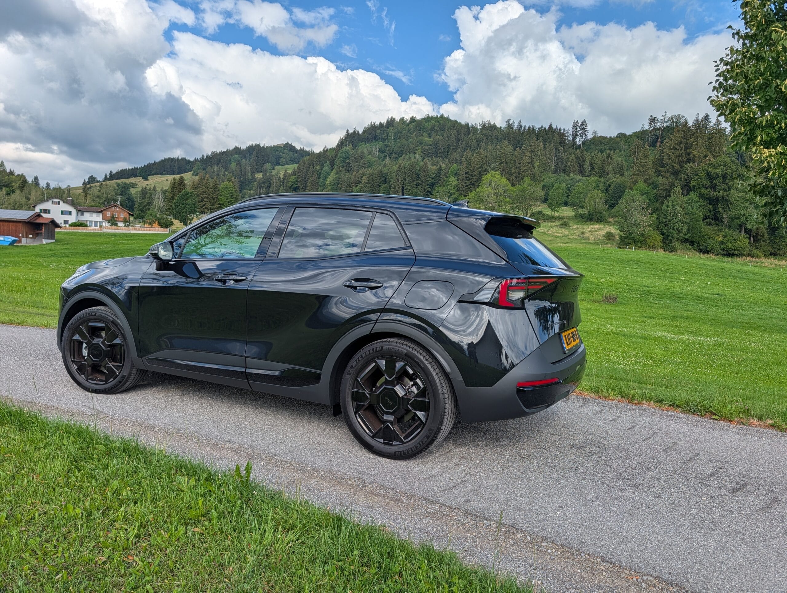 Zwarte Kia Sportage geparkeerd langs een weg in een groen berglandschap