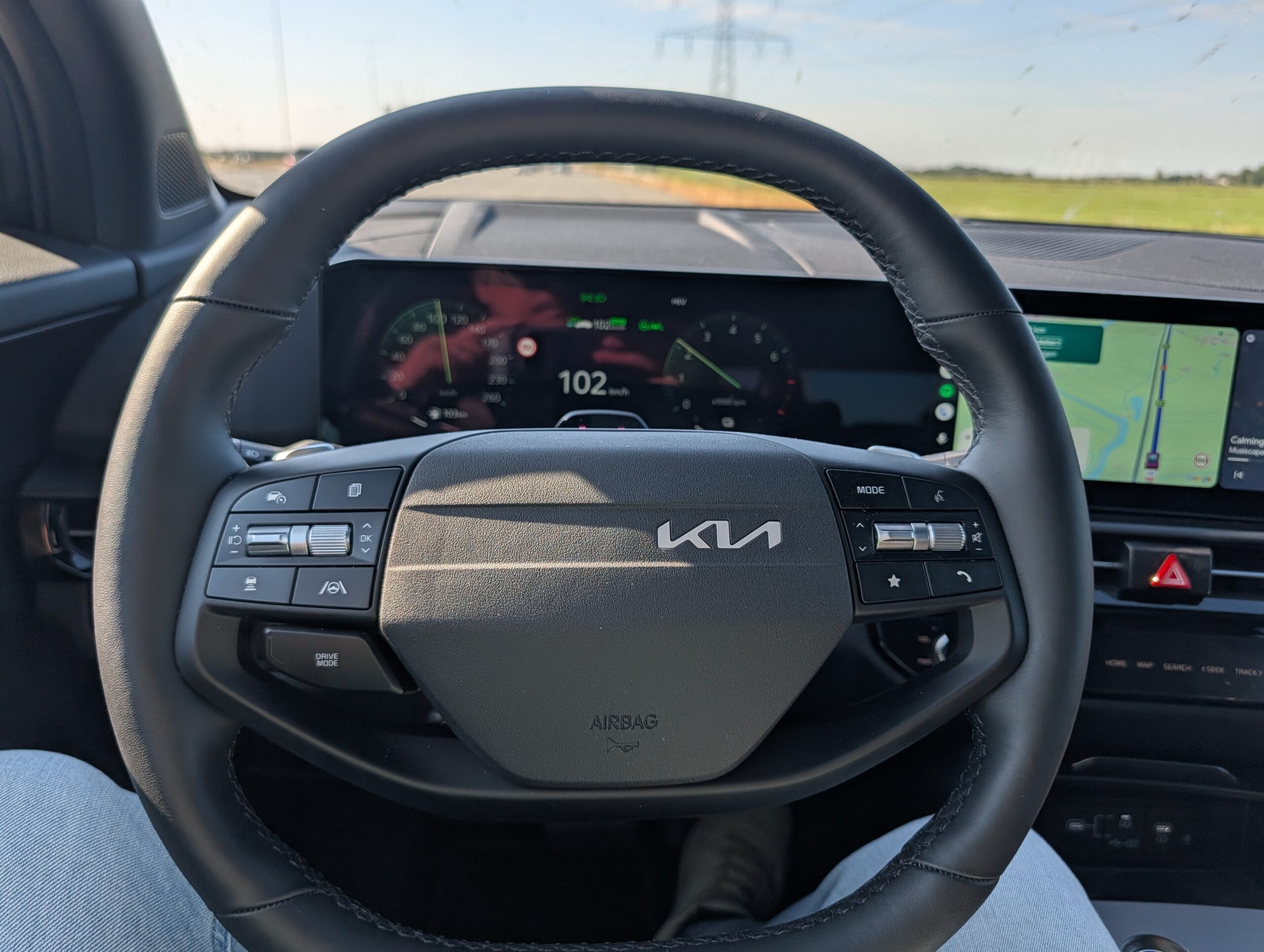 Bestuurdersstoelperspectief met het Kia-stuurwiel en het digitale dashboardpaneel met navigatie