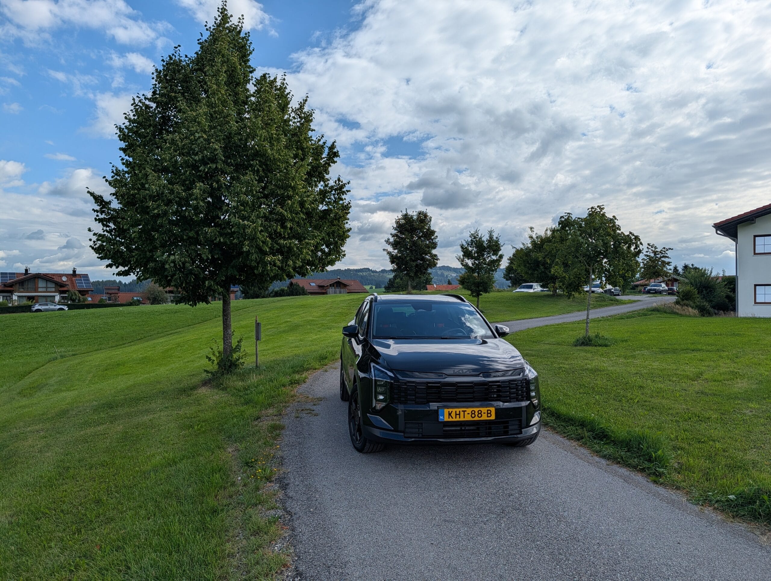 Zwarte Kia Sportage op een landweg tussen groene heuvels in een bergachtig landschap
