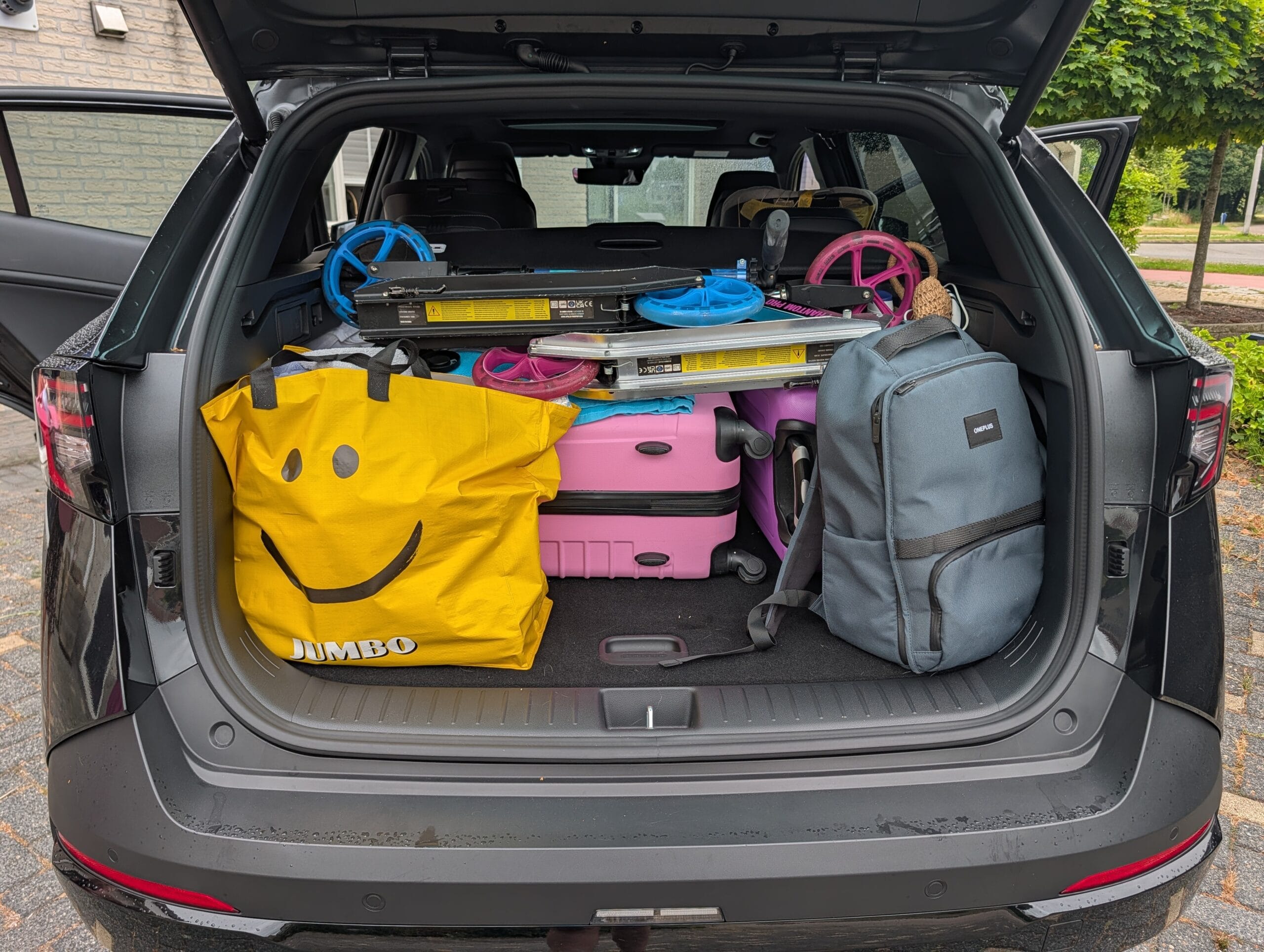 Volgepakte kofferbak van de Kia Sportage met koffers, een gele tas, een rugzak en opgevouwen steps