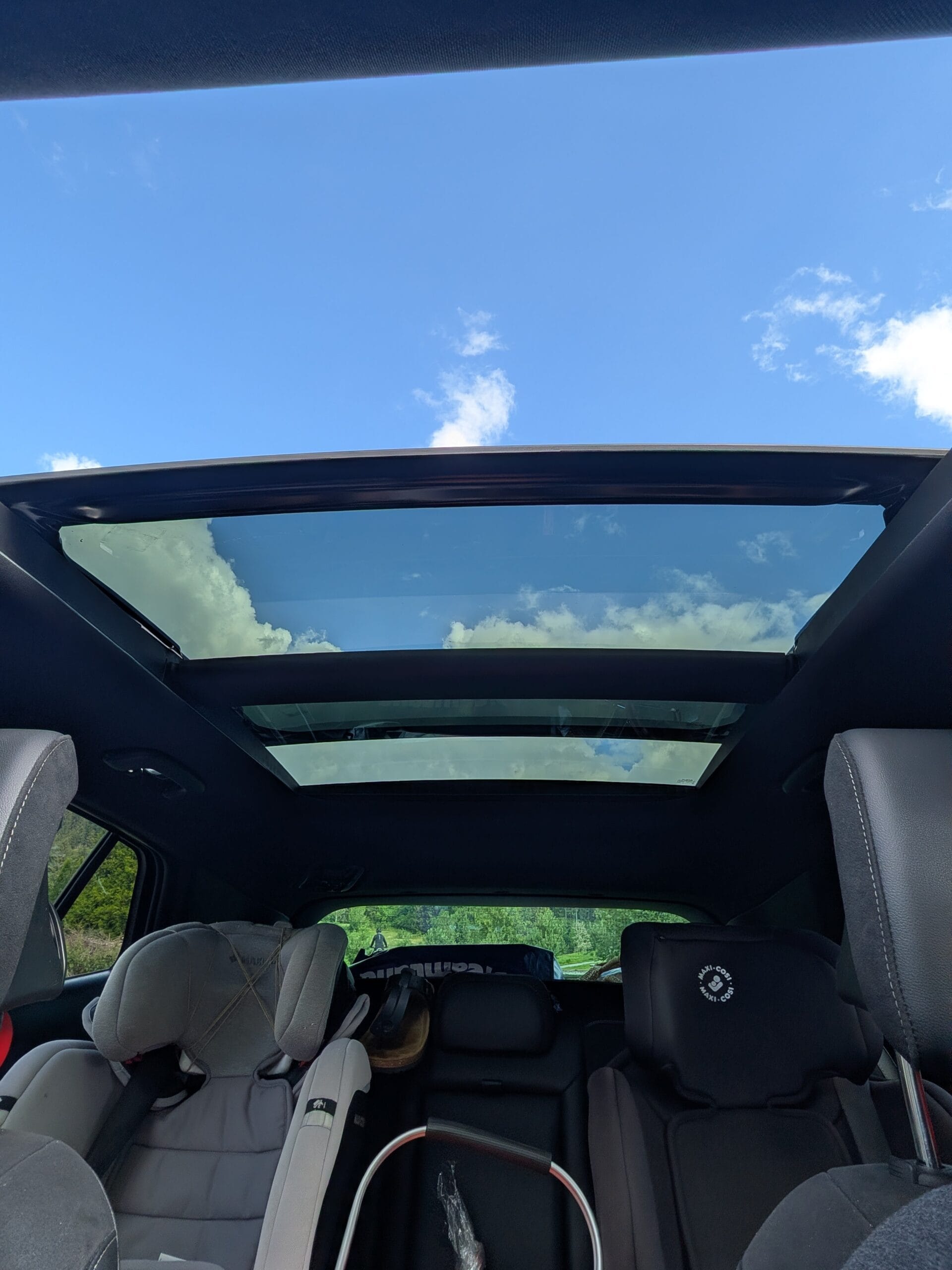 Uitzicht vanuit het interieur van de auto omhoog door het grote glazen panoramadak naar een blauwe lucht met wolken