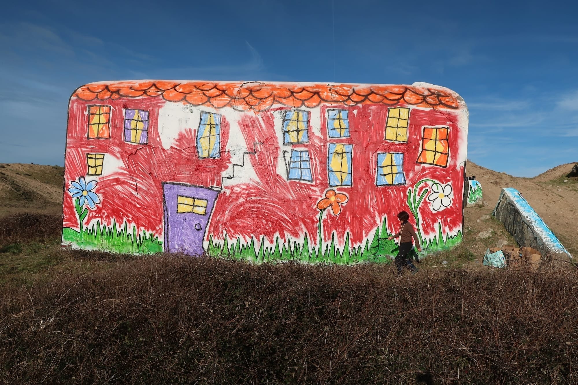 Een betonnen bunker in de duinen, beschilderd als een rood huis in de stijl van een naïeve kindertekening